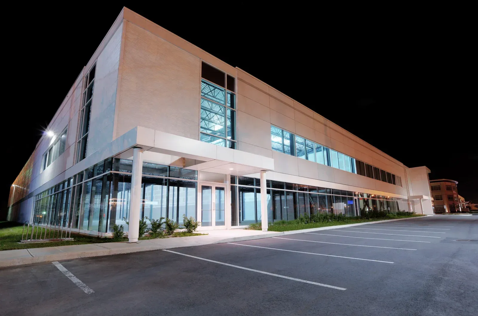 Modern commercial building with glass windows, lit up at night, parked cars.