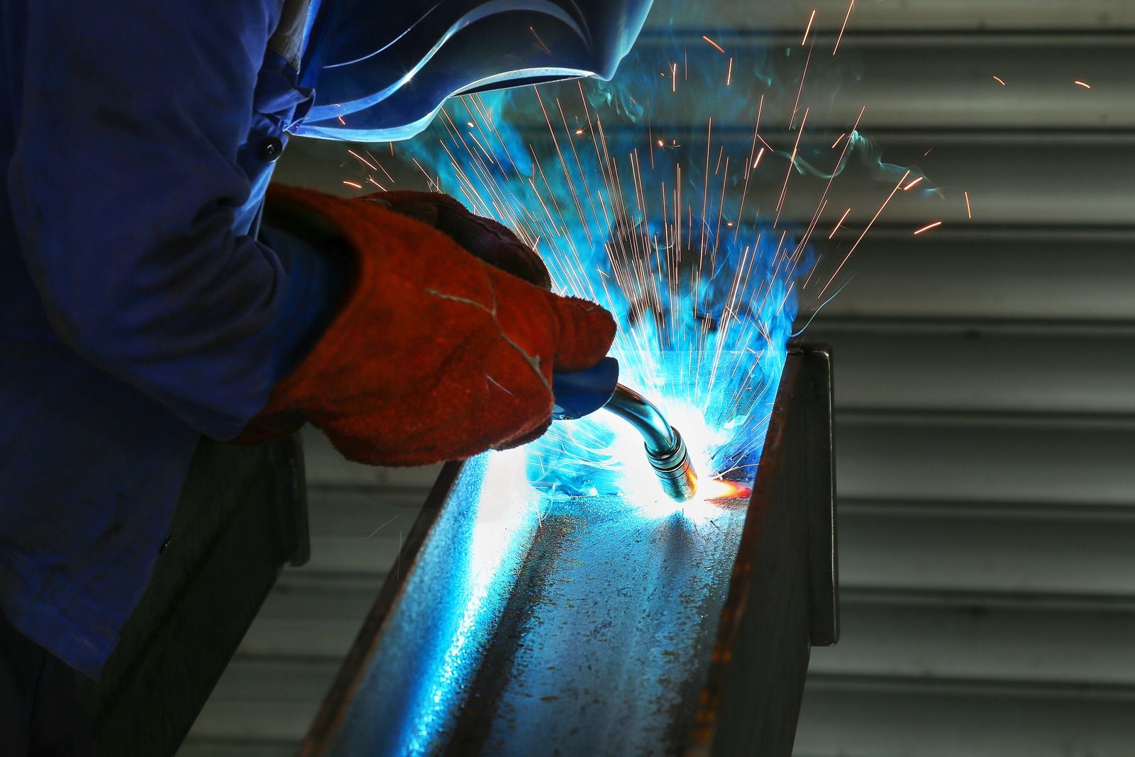 Welder in blue uniform and red gloves welding metal, bright sparks flying.