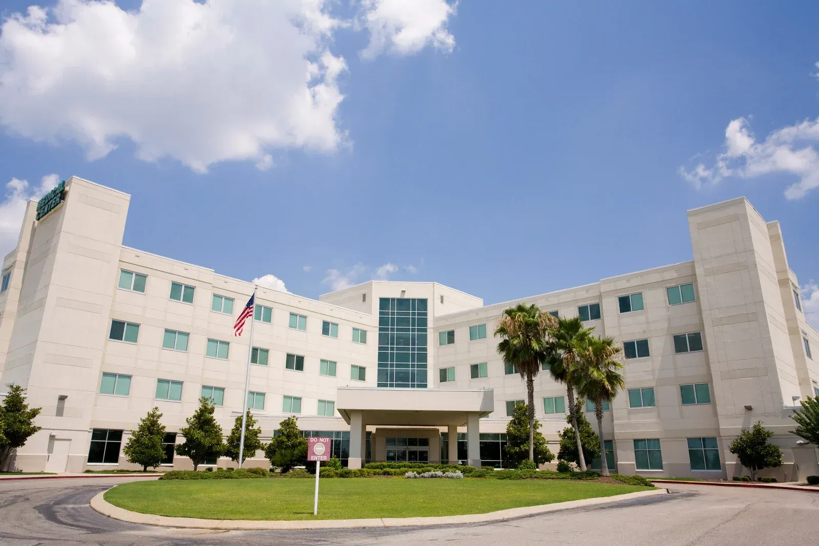Hospital building with American flag, palm trees, and a sunny sky.