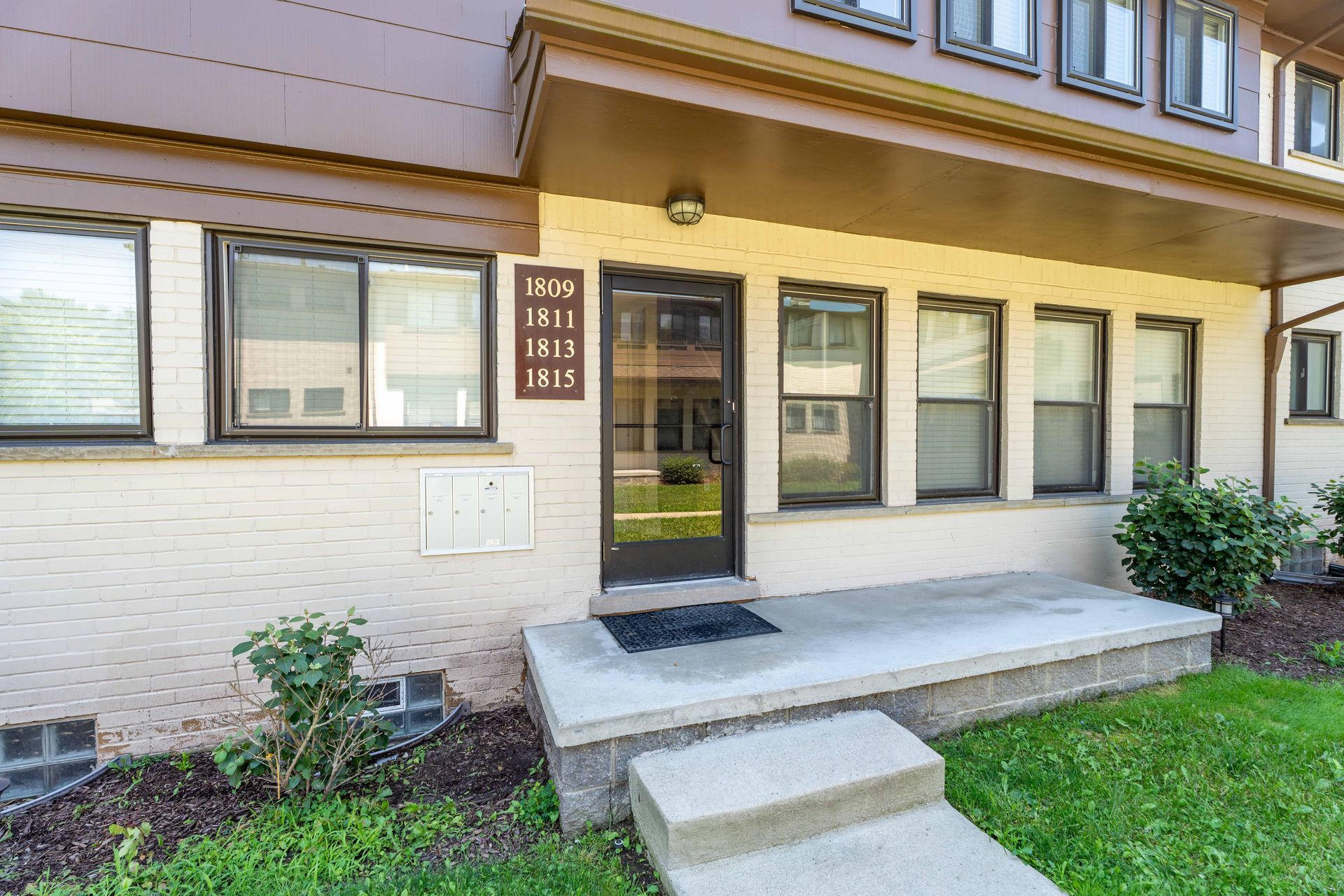 Exterior of an apartment building with a dark door, windows, and a small porch.