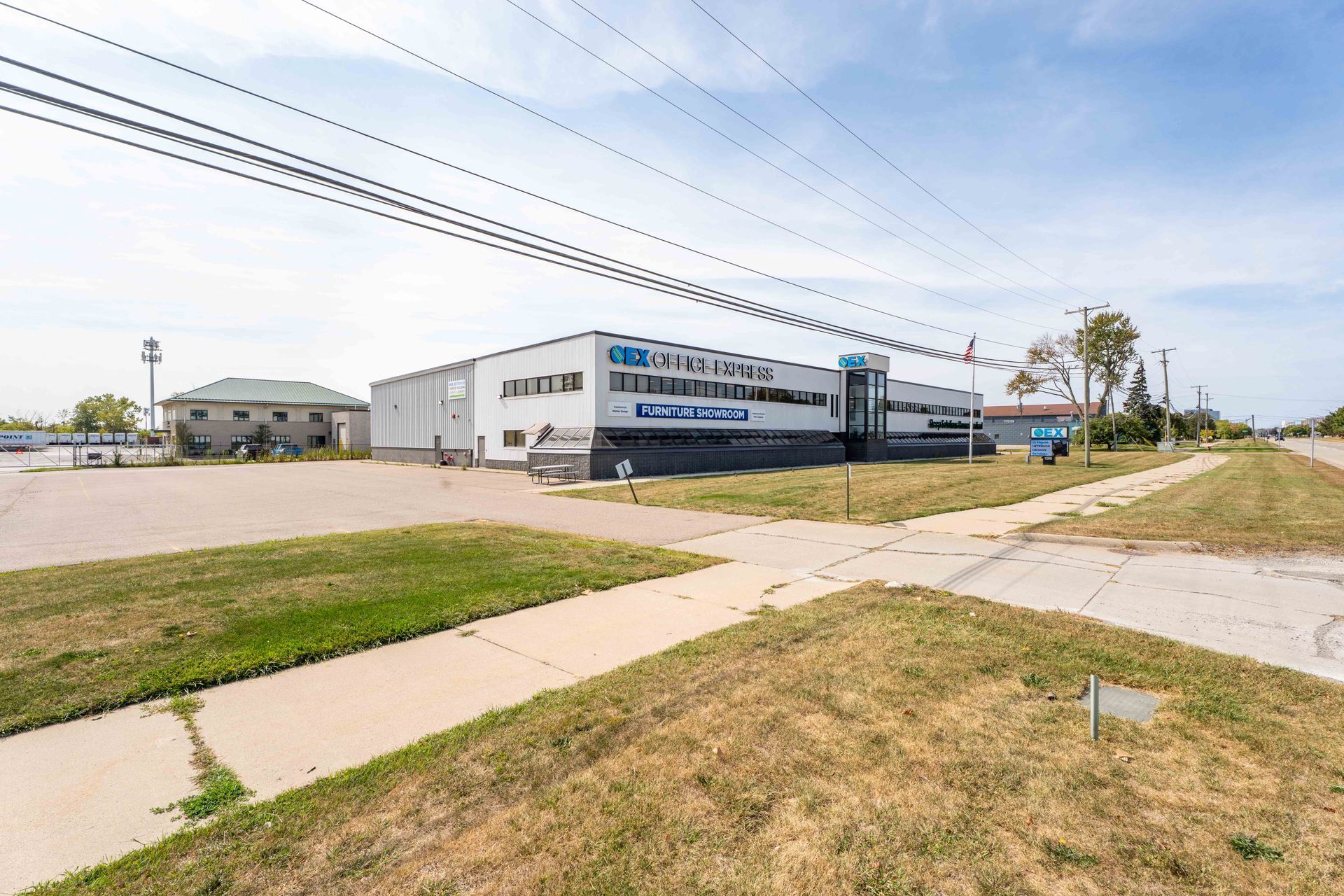 Exterior view of a commercial building with a grass lawn in front, viewed from a street corner on a sunny day.