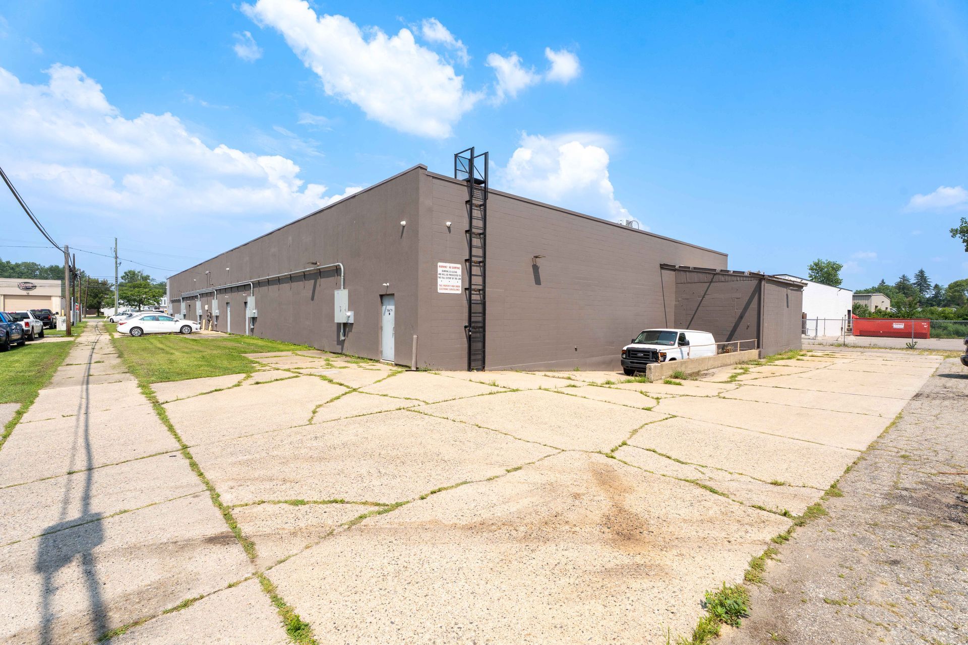 Brown industrial building with cracked concrete lot, white van, blue sky.