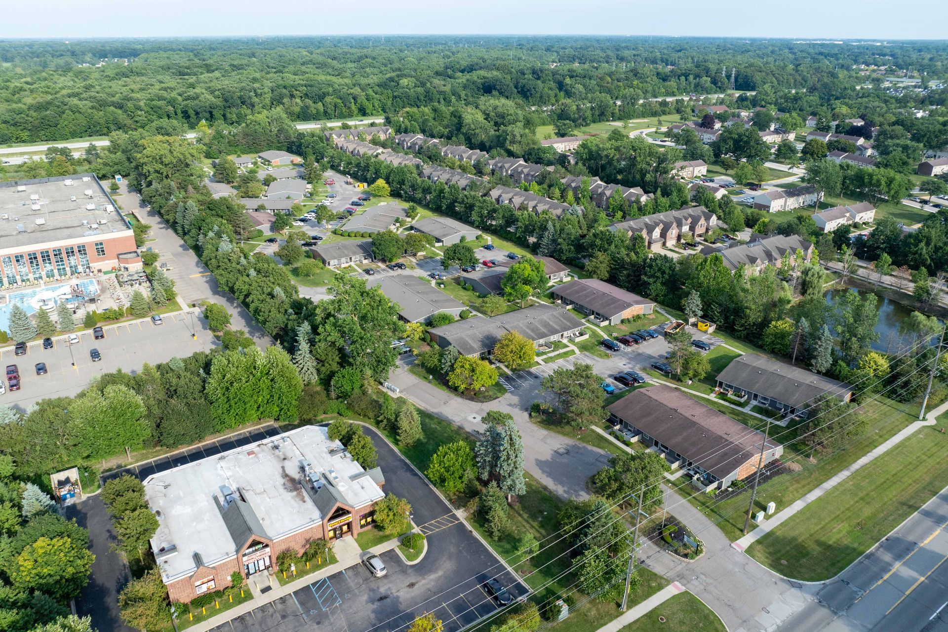 Aerial view of a residential area with buildings, trees, parking lots, and a road.