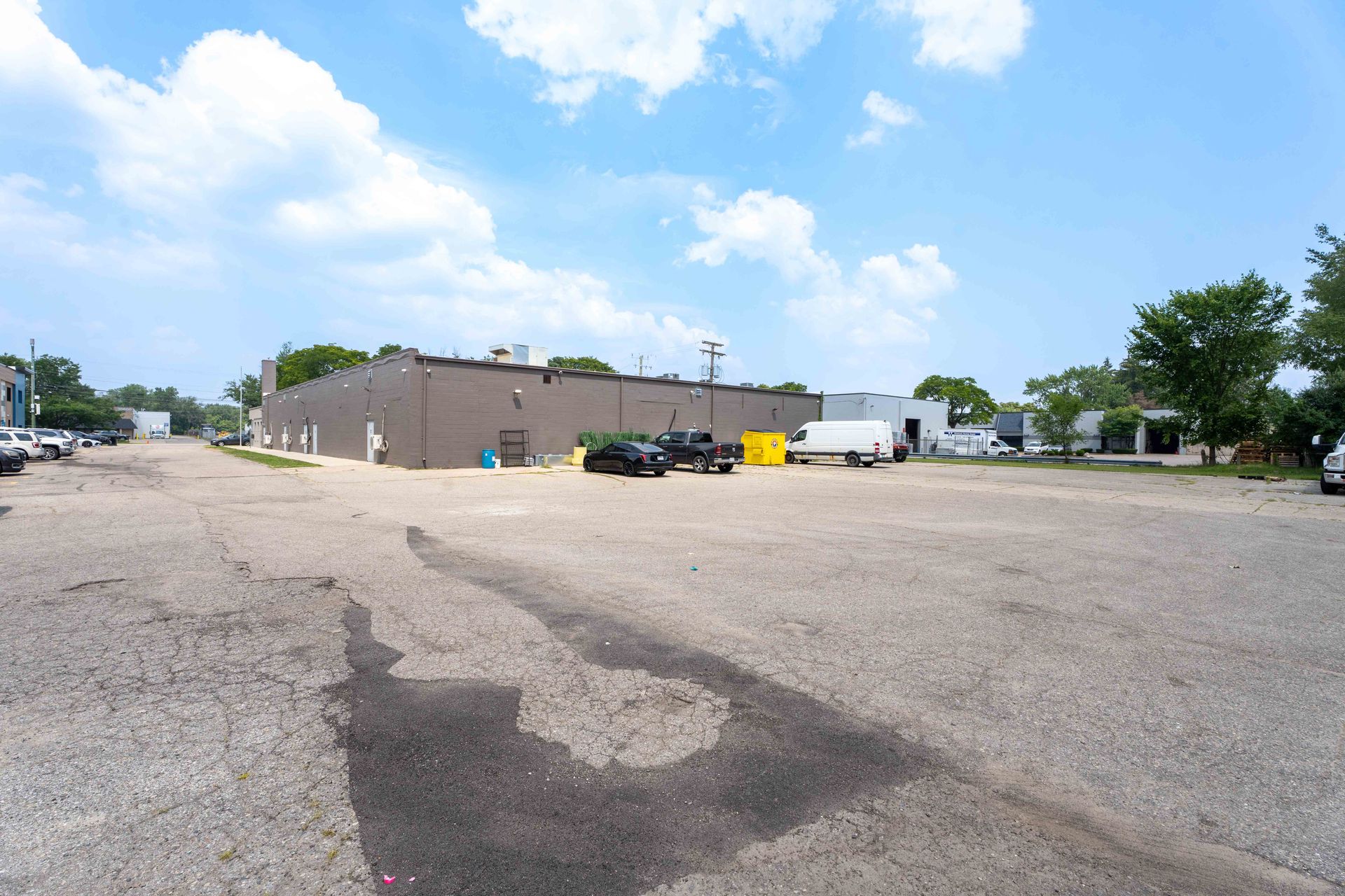 Wide outdoor shot of an asphalt parking lot leading to a brown building under a cloudy sky.