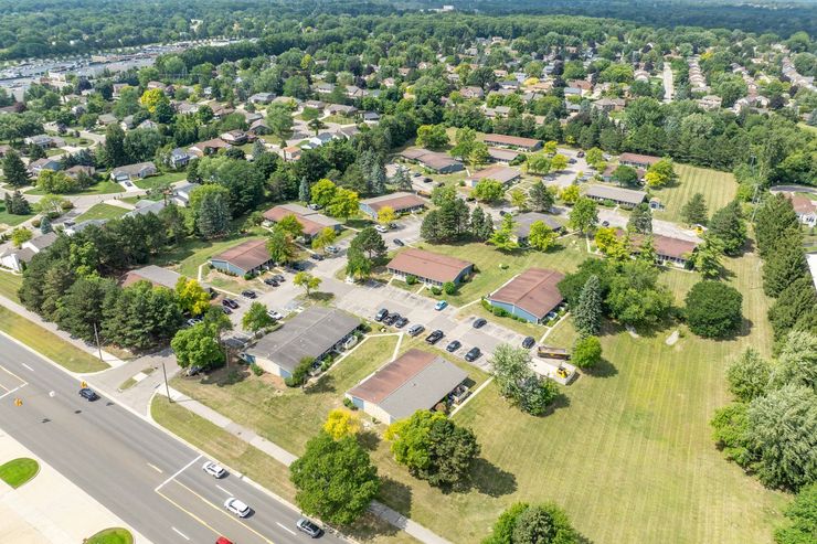 Aerial view of a suburban neighborhood with rows of houses, green trees, and a road.