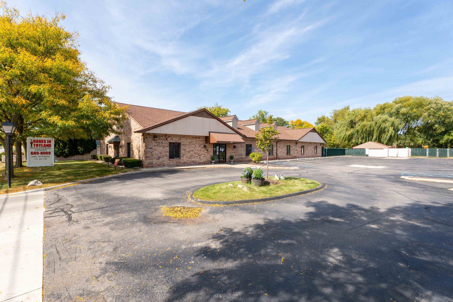 Brick building with a circular driveway and small landscaped island, under a blue sky.