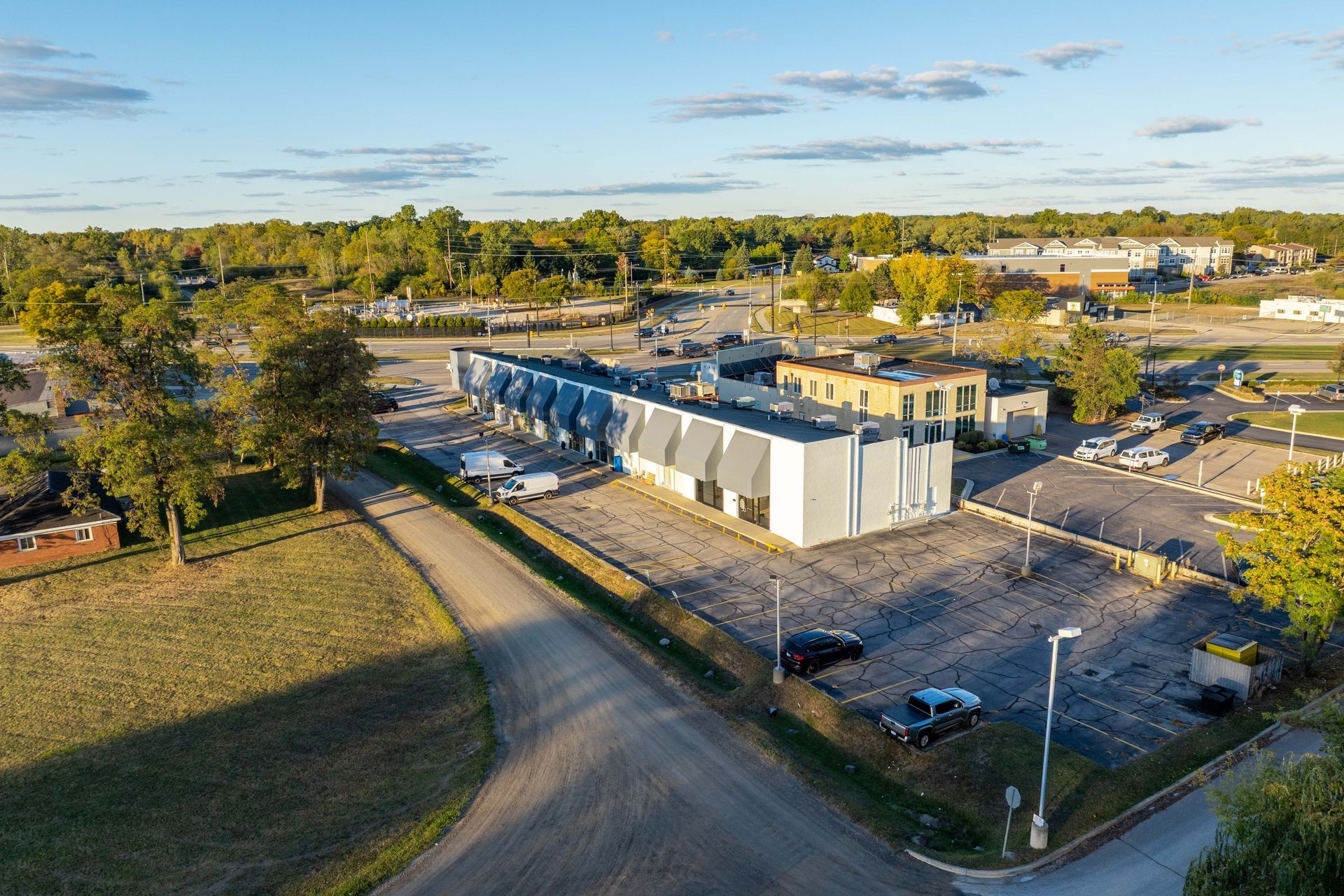 Aerial view of a gray industrial building with a large parking lot on a sunny day.