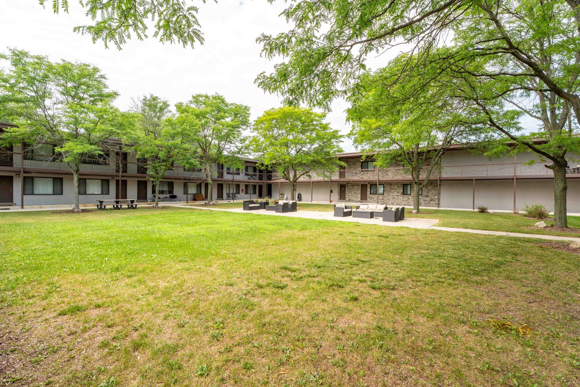 Lawn and patio furniture in a courtyard surrounded by a two-story building and trees.