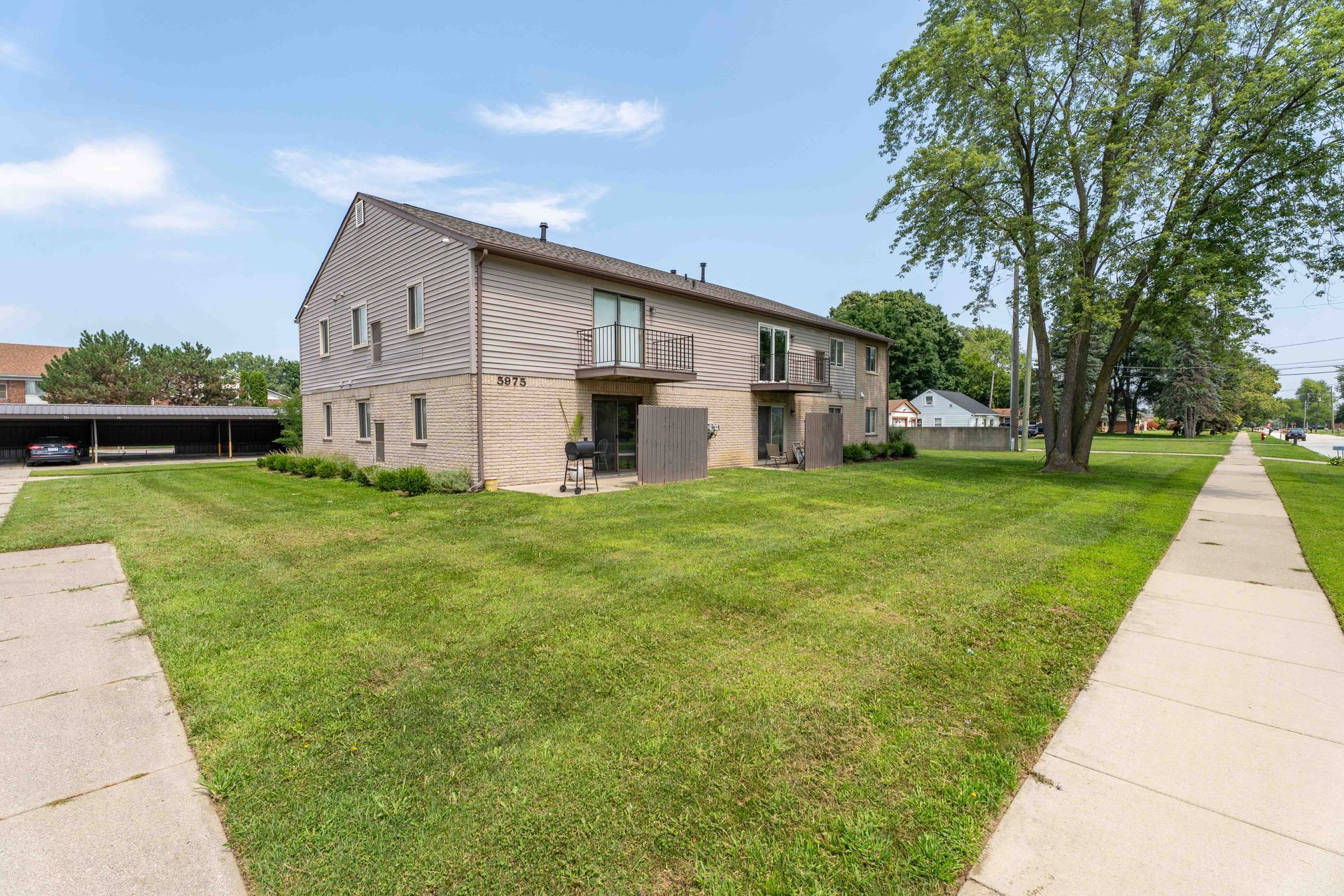 Two-story beige apartment building with green lawn and sidewalk on a sunny day.