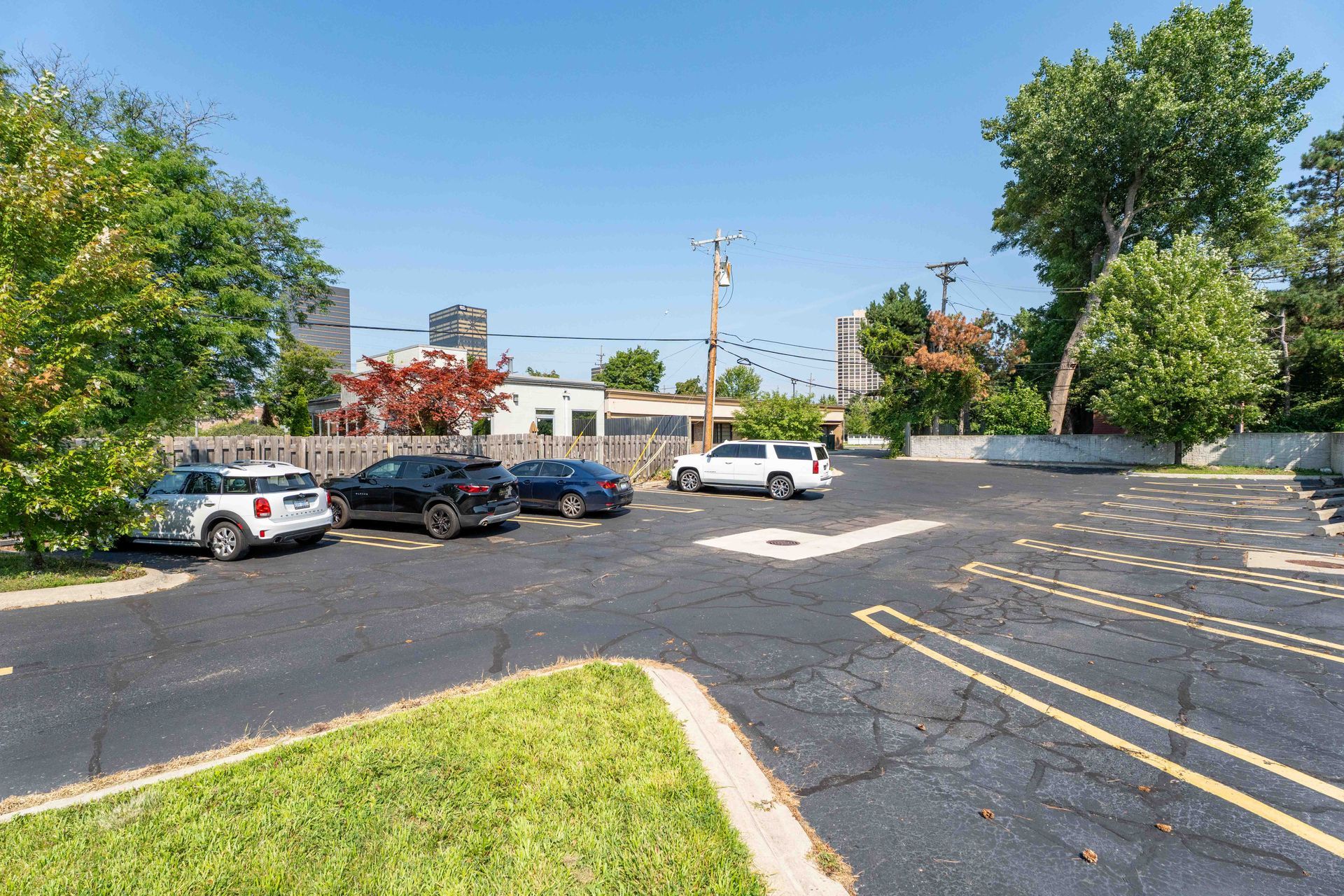 Parking lot with several cars, trees, and a building on a sunny day.