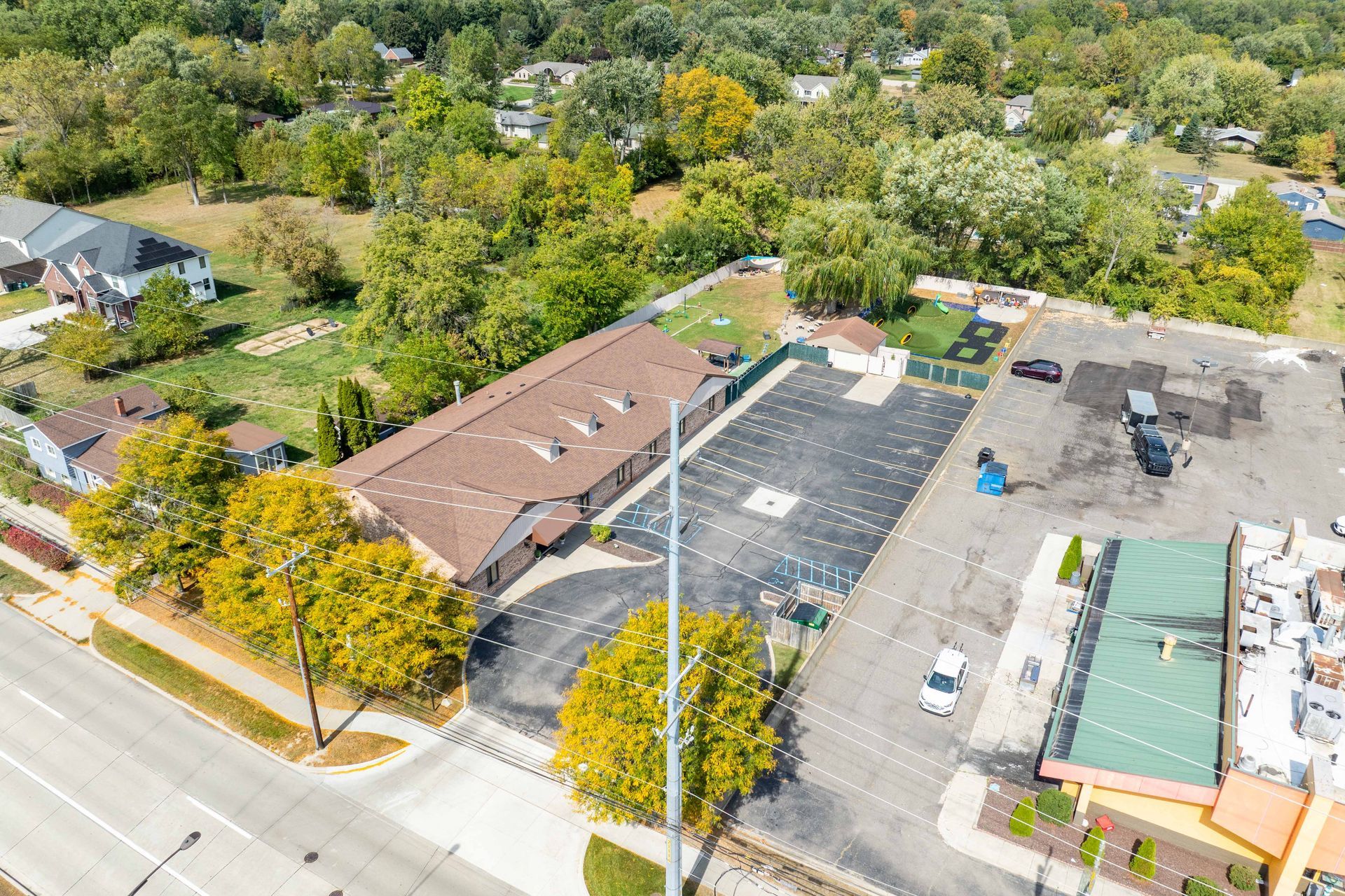 Aerial view of a commercial building with large parking lot, surrounded by trees and residential areas.