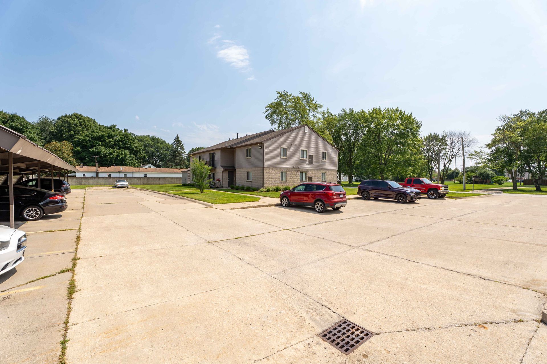 Apartment building with parking lot, cars parked, trees, and blue sky.