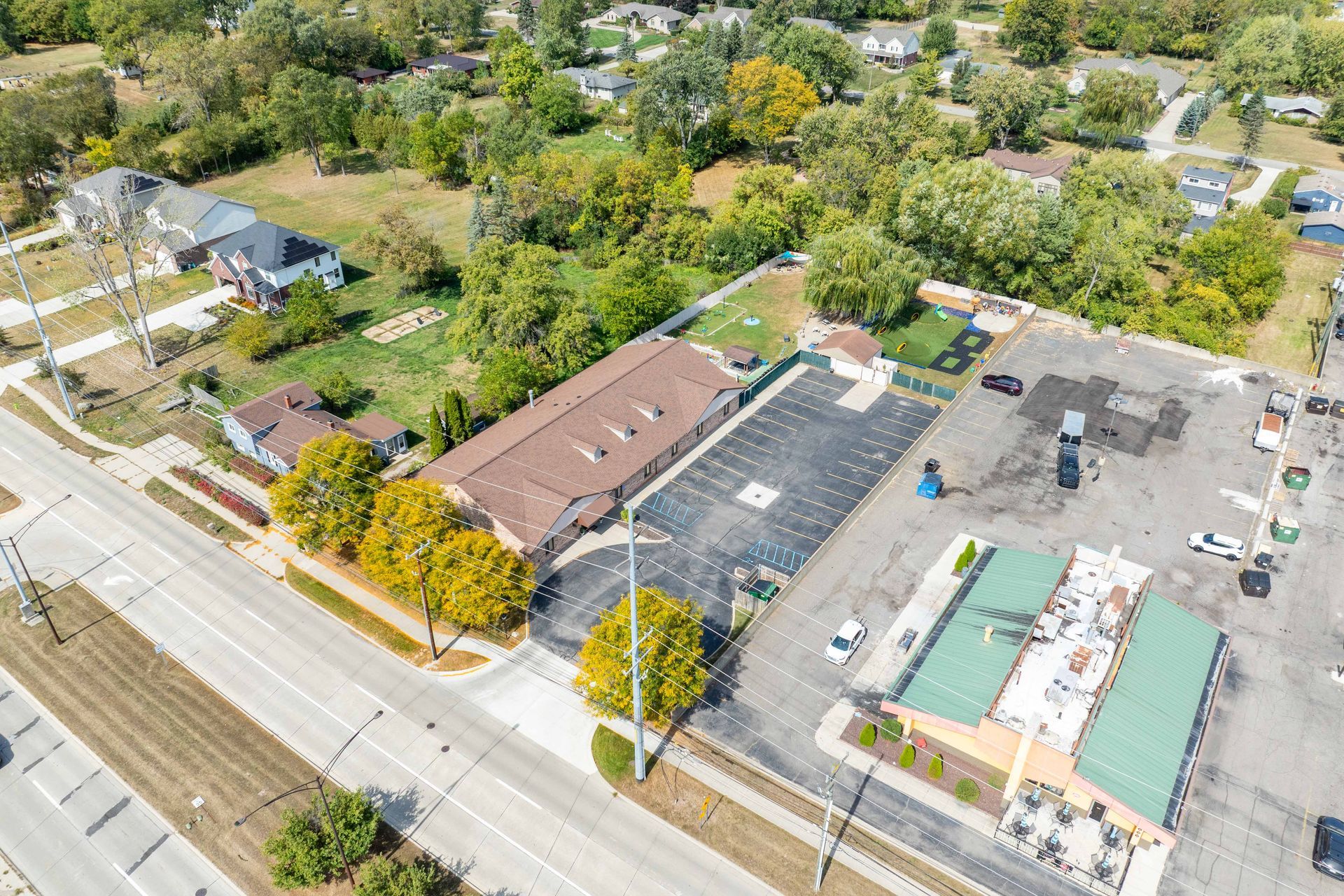 Aerial view of a commercial area with a motel, parking lot, restaurant, and houses.