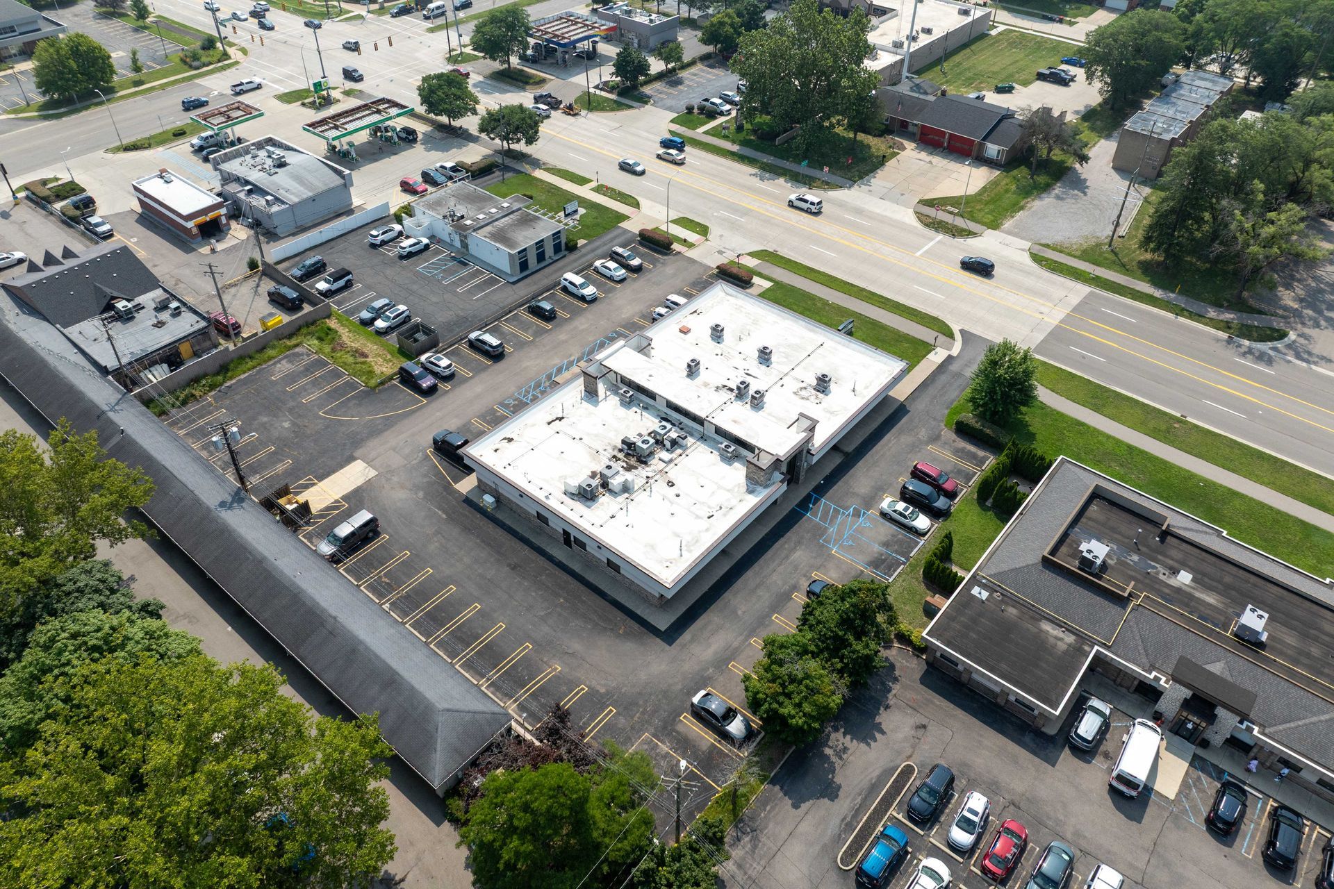Aerial view of commercial buildings with parking lots and a road. Green trees border some buildings.