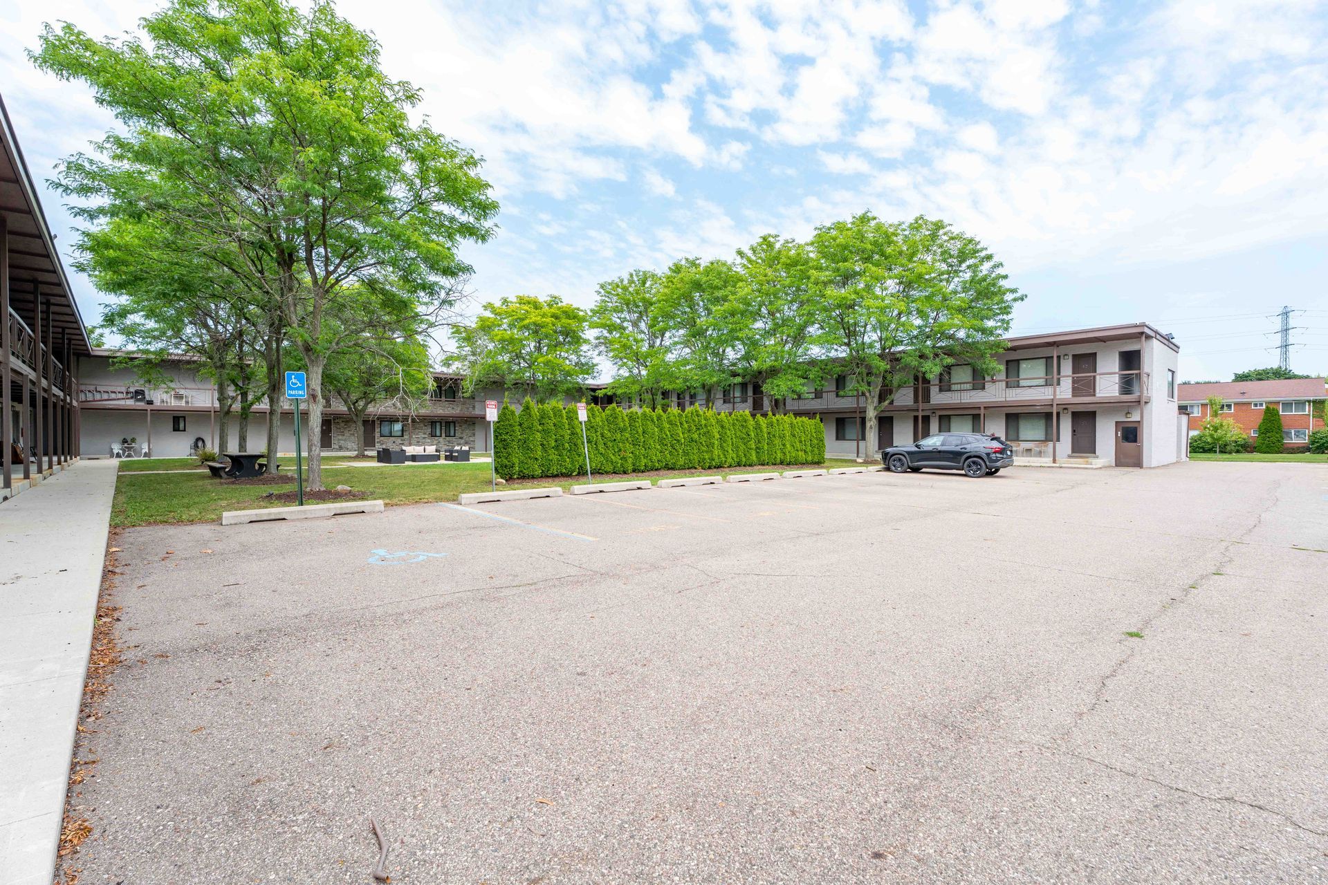 A motel with a large empty parking lot and trees under a cloudy sky.