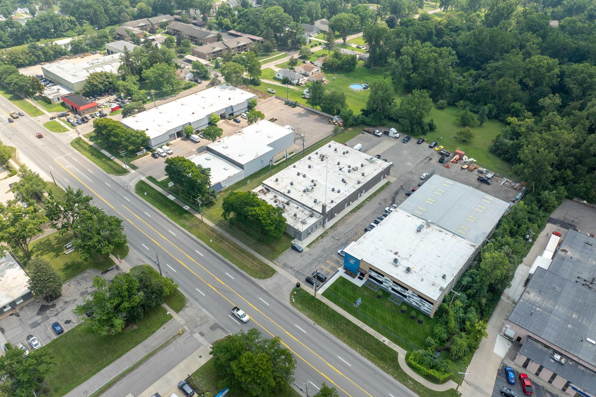 Aerial view of commercial buildings along a road with trees and a grassy area.