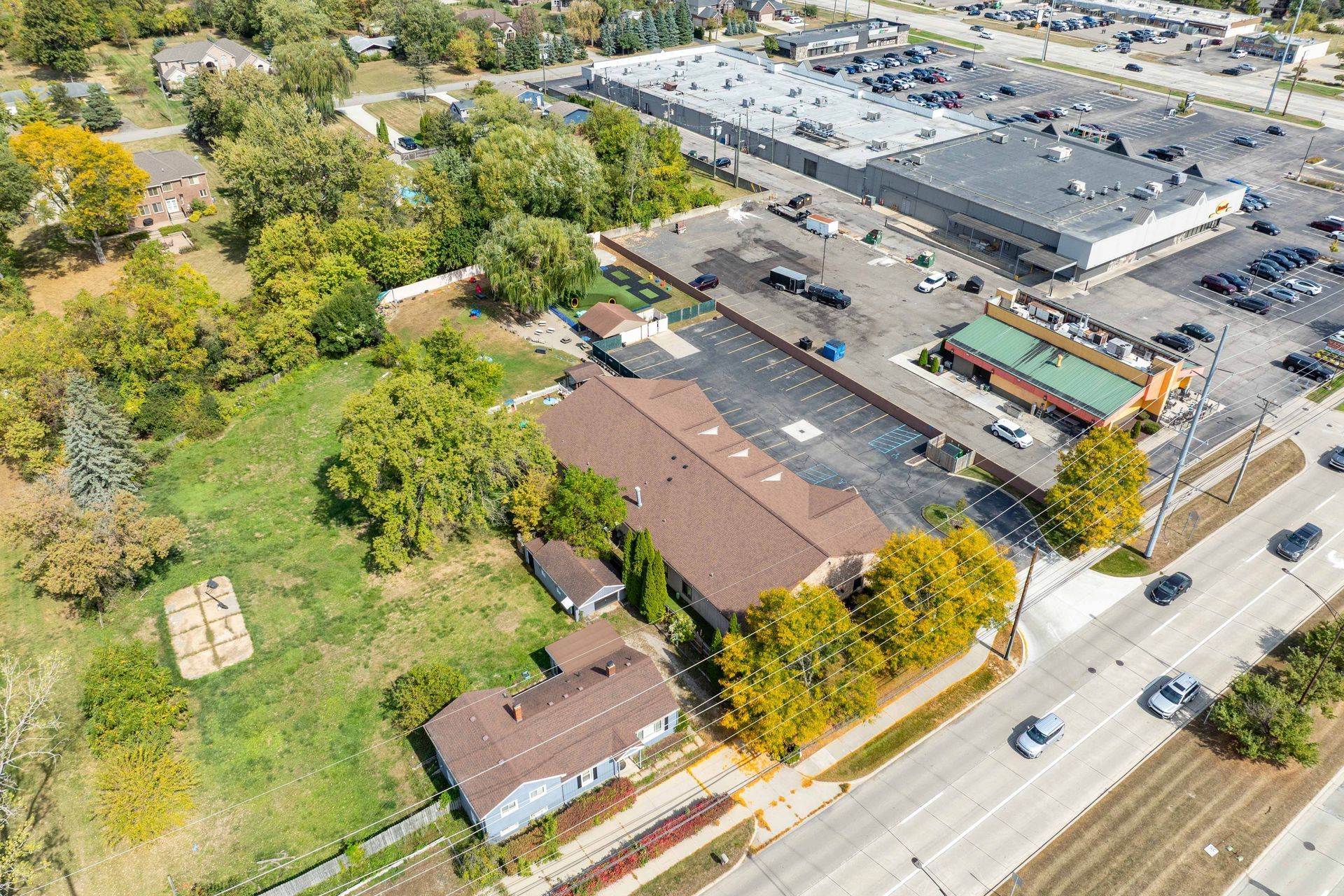 Aerial view: Buildings near a road with cars, a parking lot with a large store, and green trees.