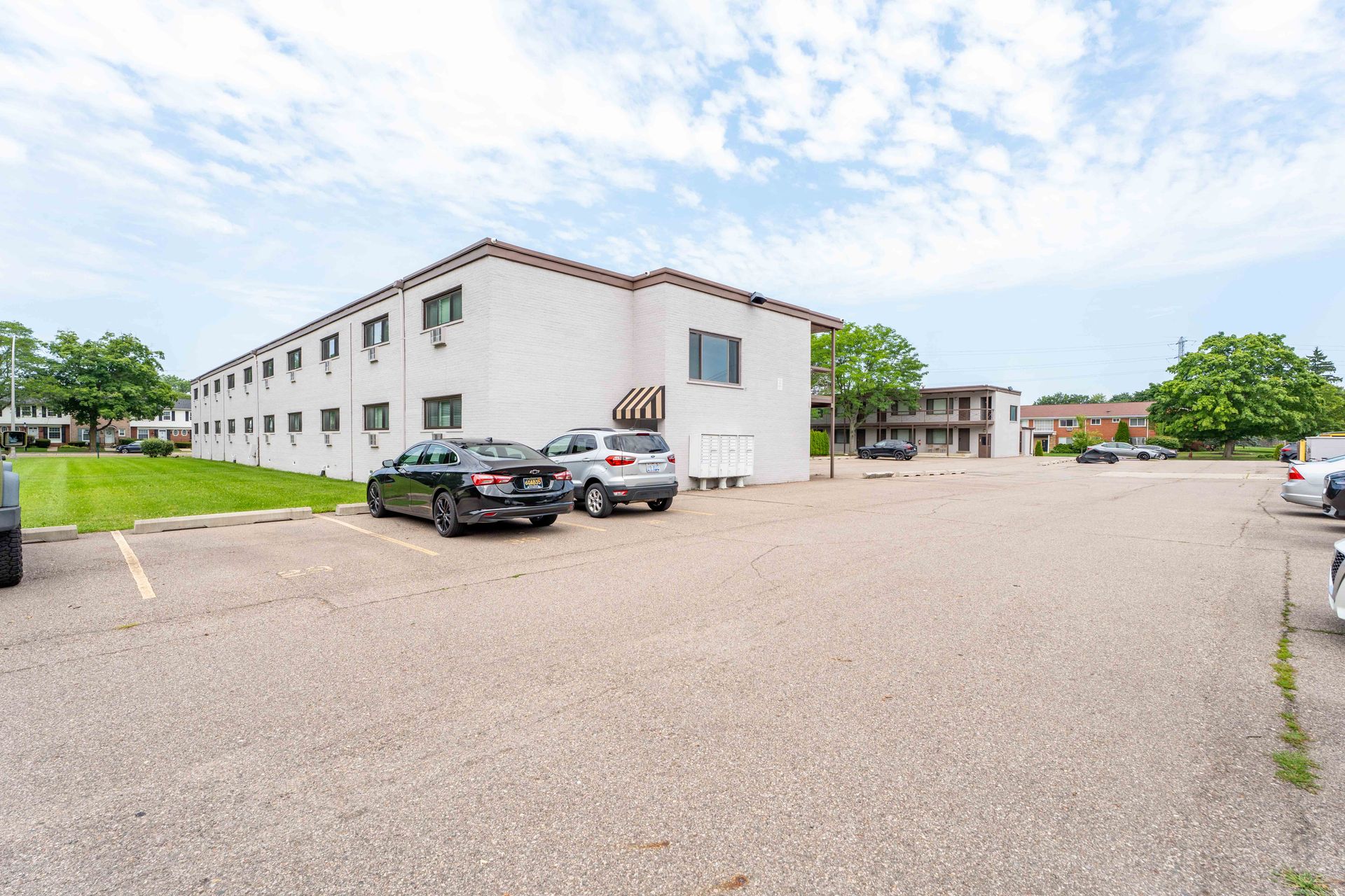 Exterior view of a white two-story building with a parking lot. Cars are parked in front. Cloudy sky.