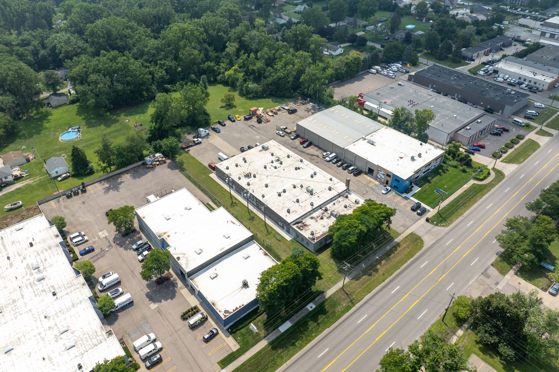 Aerial view of industrial buildings with parked cars, trees, and a multi-lane road.