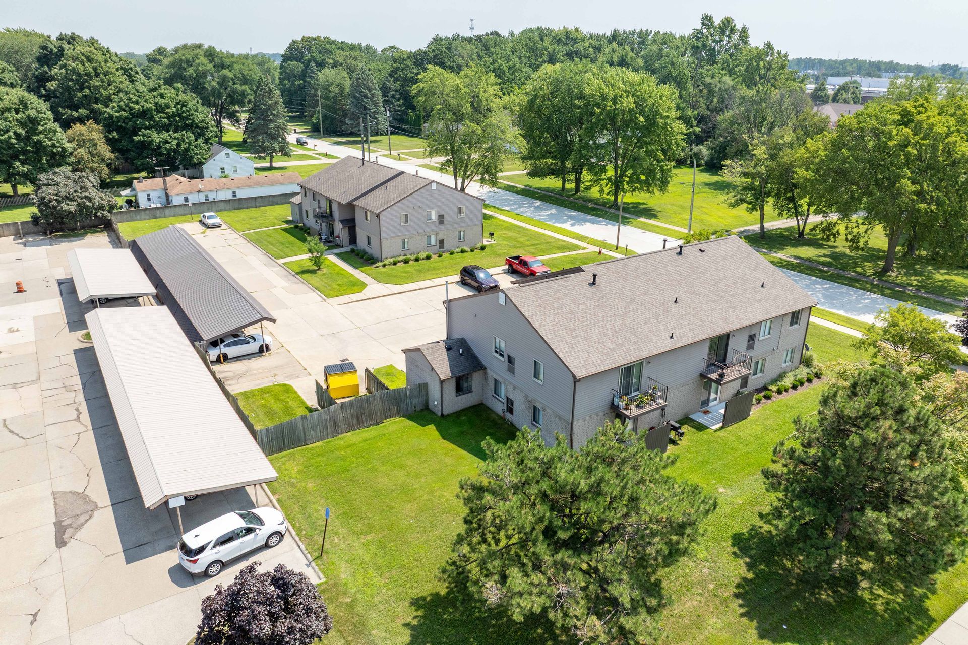 Aerial view of apartment complex with gray buildings, carport, and green lawn.