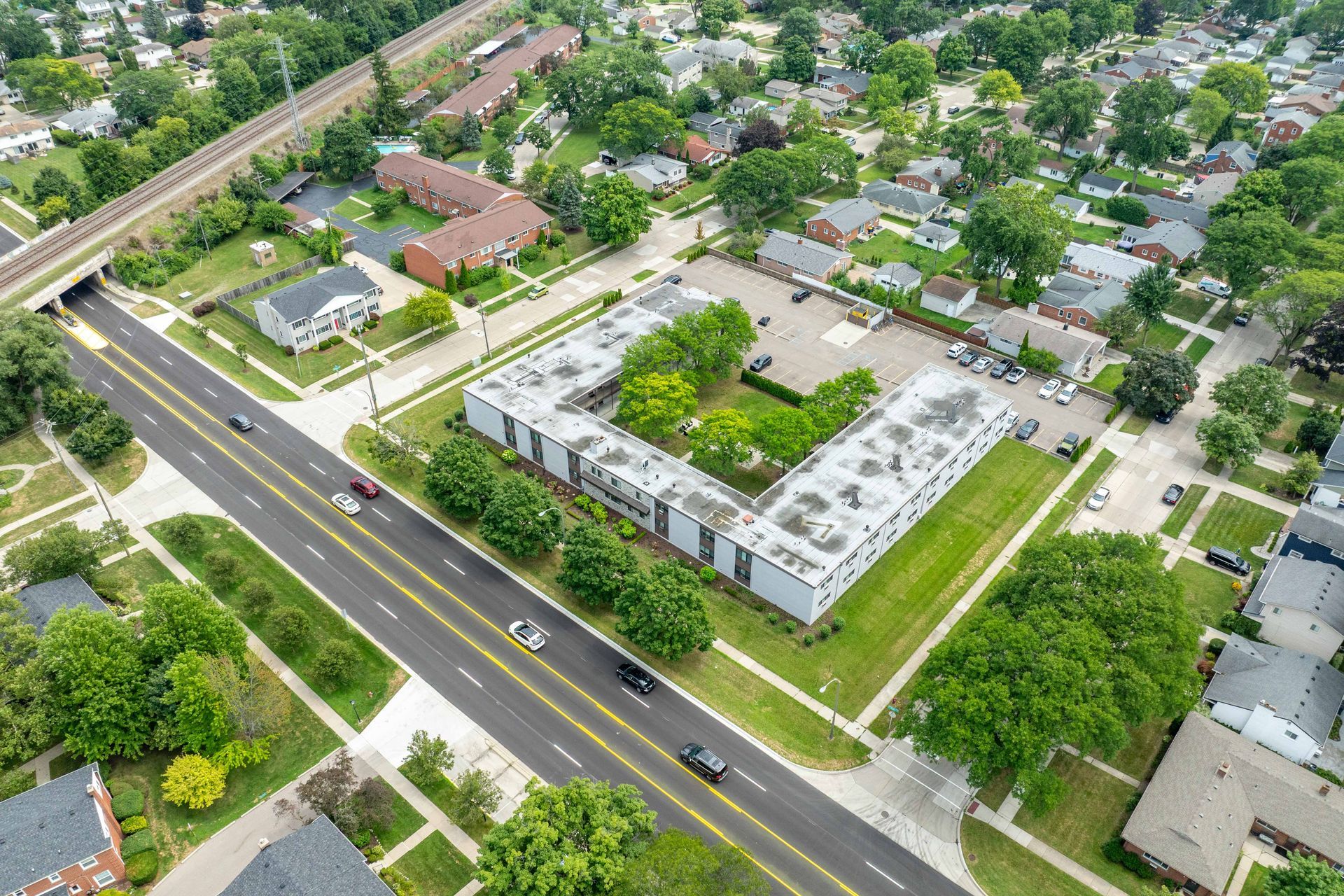 Aerial view of a U-shaped apartment complex, green lawn, road, and houses.