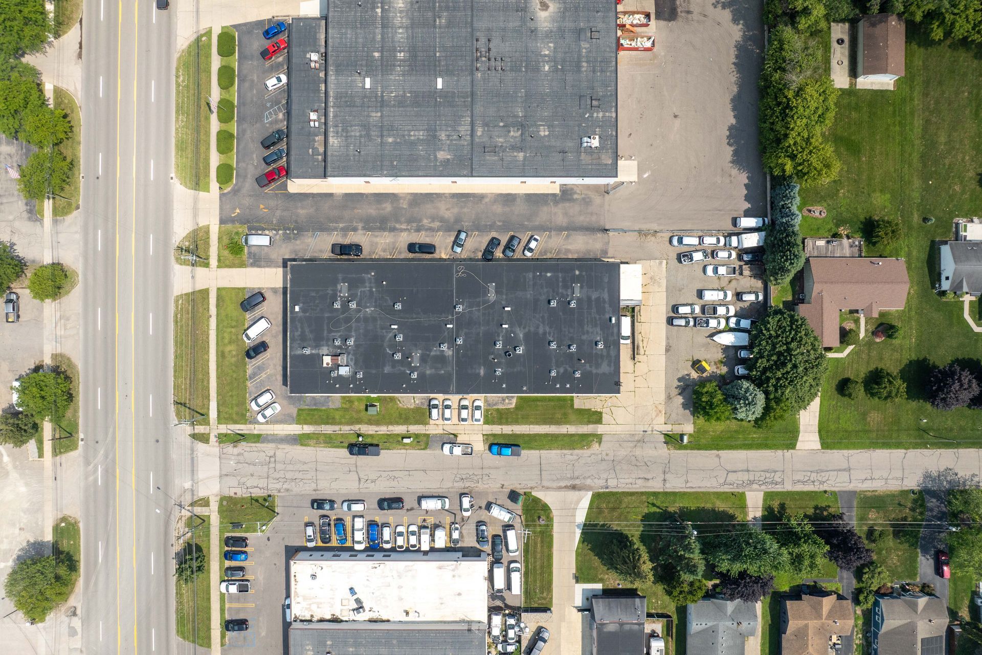 Aerial view of a commercial area with buildings, parking, and roads; some residential properties are also visible.