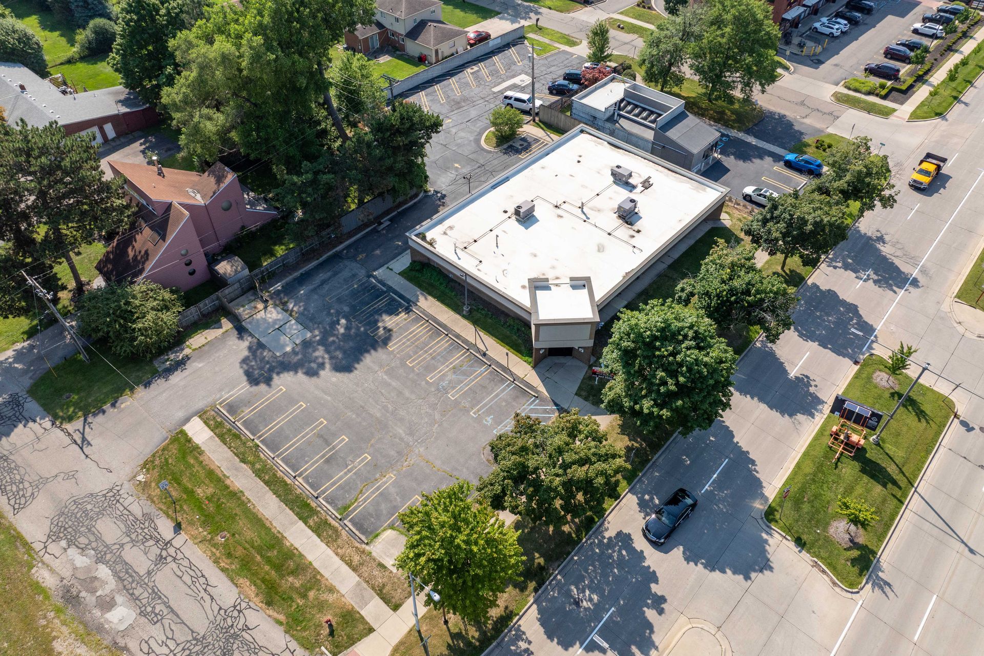 Aerial view of a building with a flat roof, surrounded by parking lots and trees.