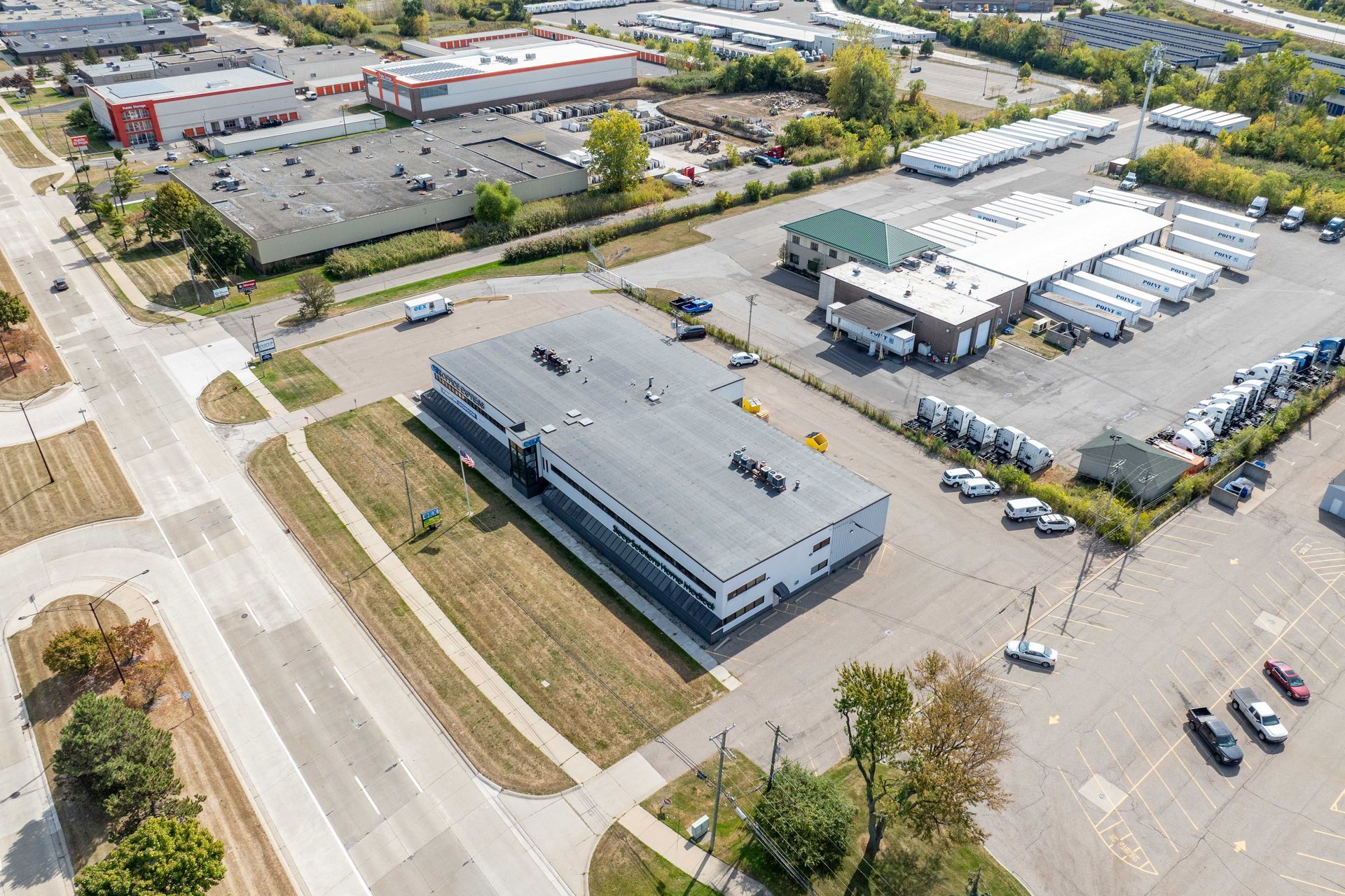 Aerial view of industrial buildings and parking lot. White trucks and cars parked.