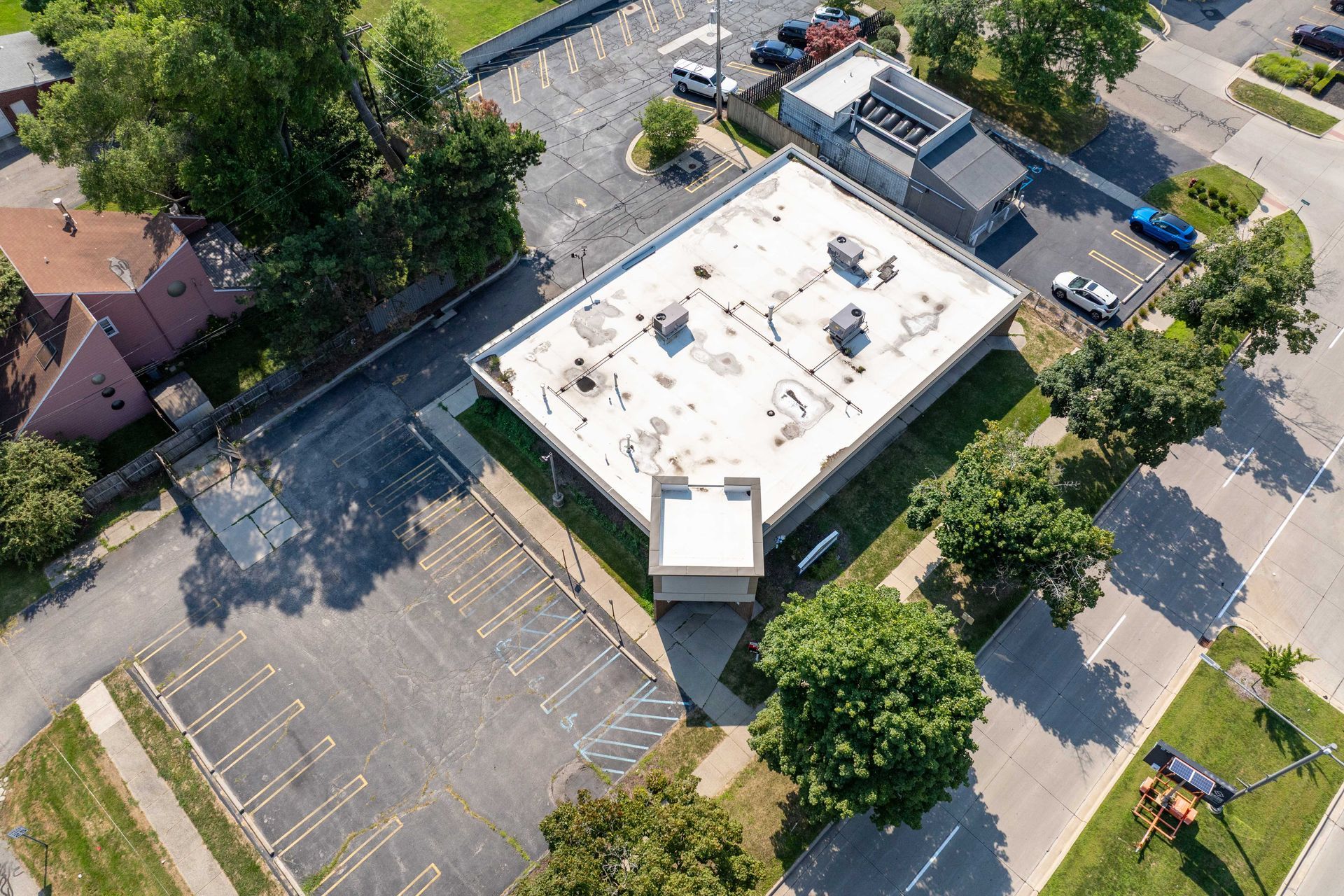 Aerial view of a rectangular building with a flat roof, surrounded by parking lots and trees.