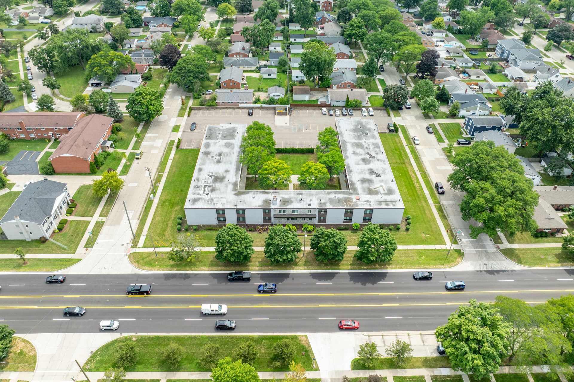 Aerial view of a rectangular building with a central courtyard surrounded by residential neighborhood and a road with traffic.