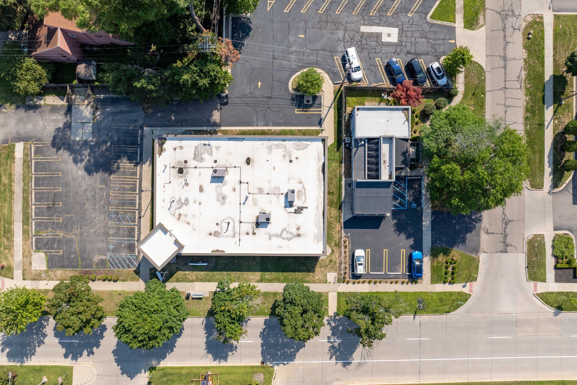 Aerial view of a commercial building with a flat roof, surrounded by parking lots and streets with cars.