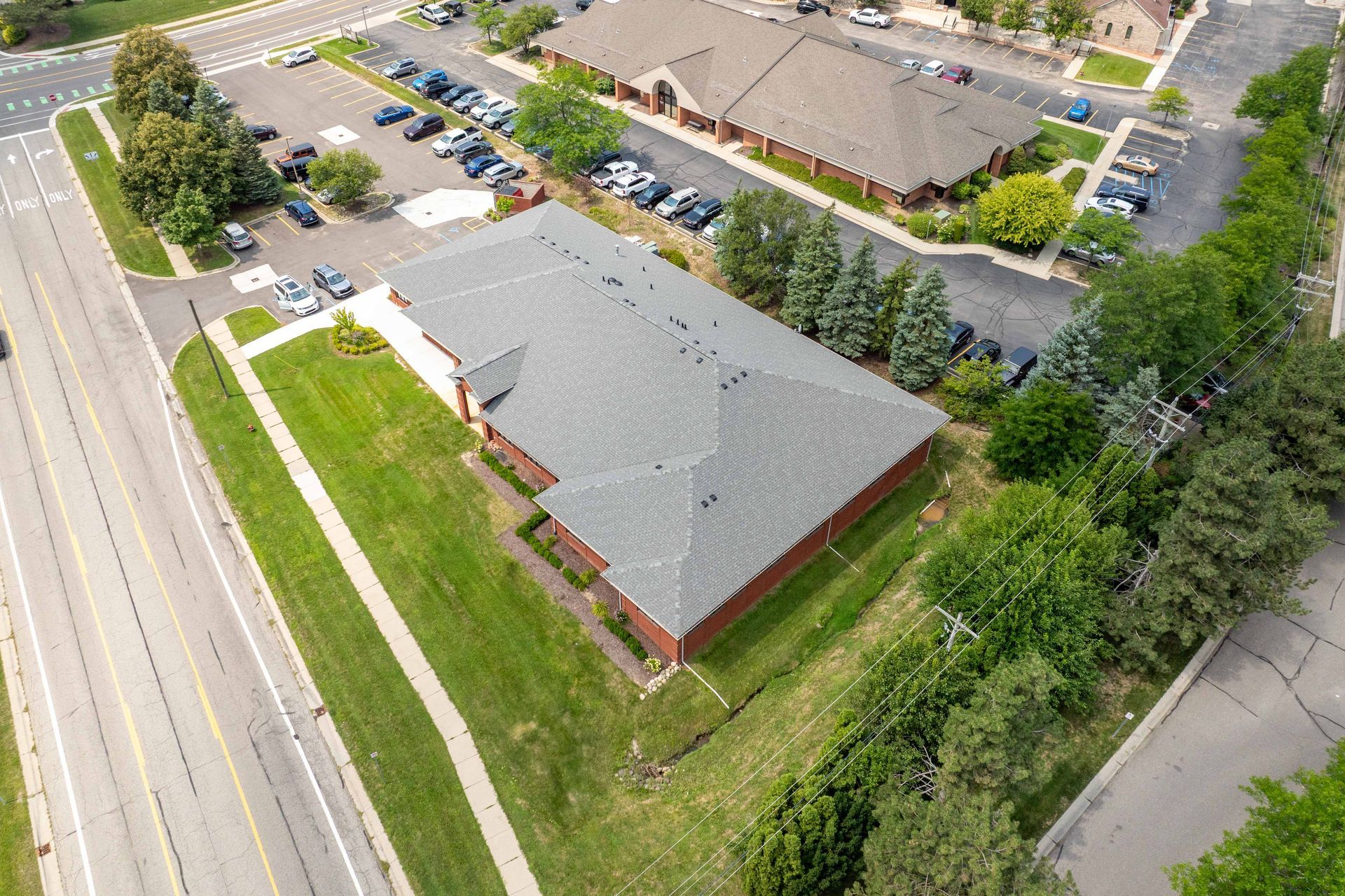 Aerial view of a one-story brick building with a dark gray roof, surrounded by parking lots, trees, and roads.