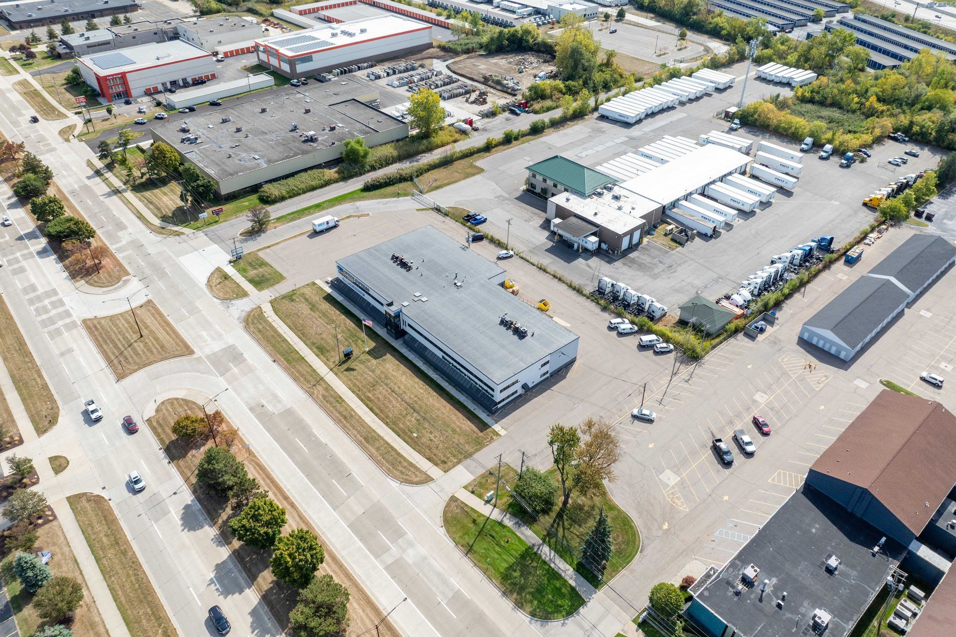 Aerial view of industrial buildings, roadways, parking lots, and vehicles in an urban setting.