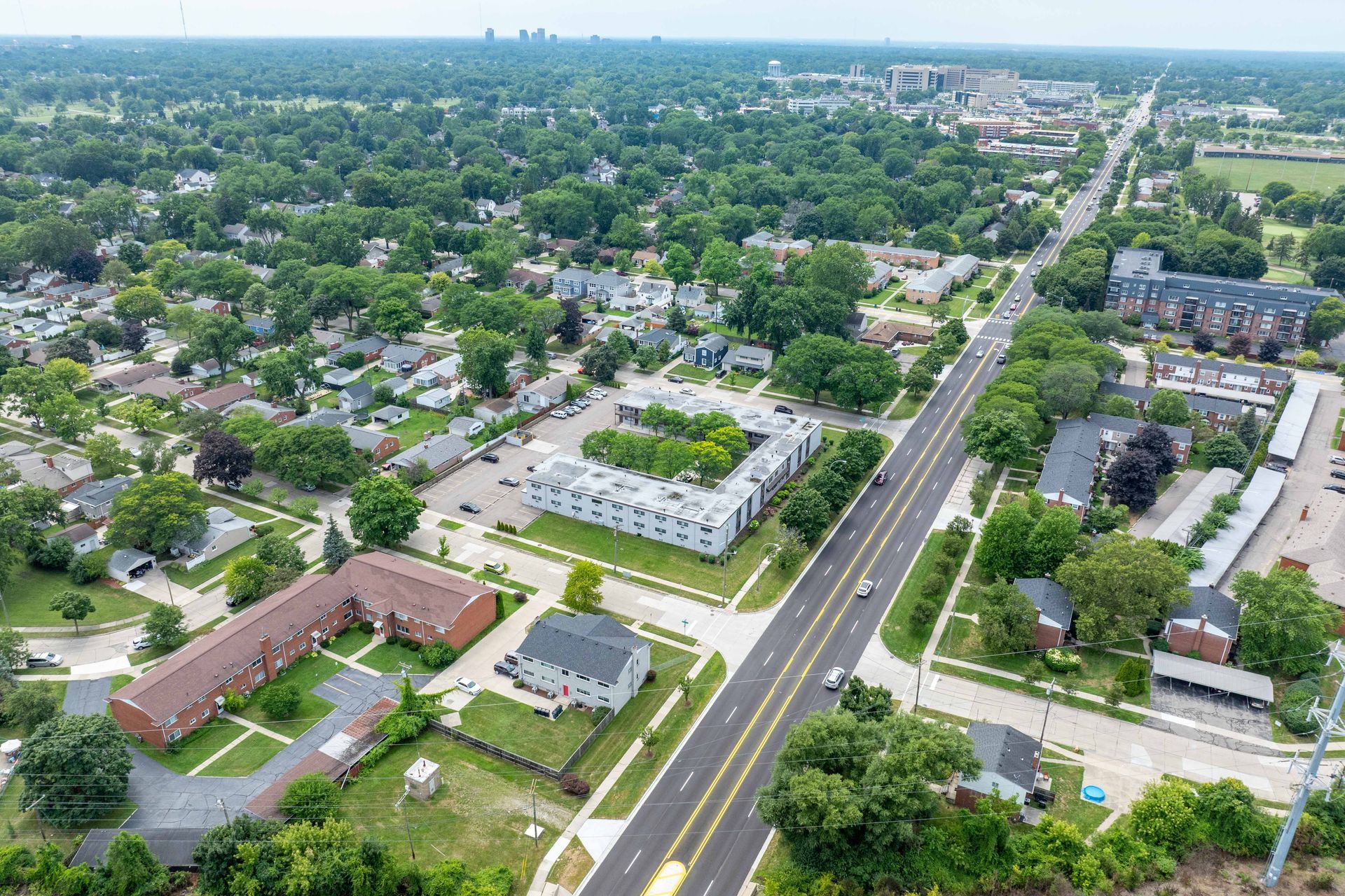 Aerial view of a suburban area with a street, buildings, and many trees on a sunny day.