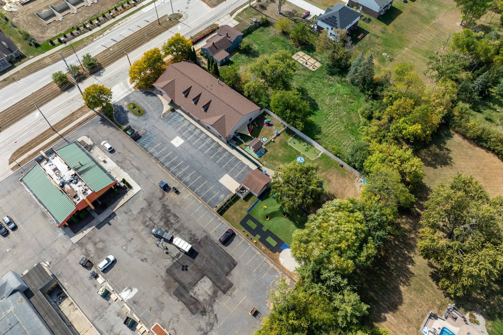 Aerial view: commercial buildings, parking lots, a road, and green spaces under a sunny sky.