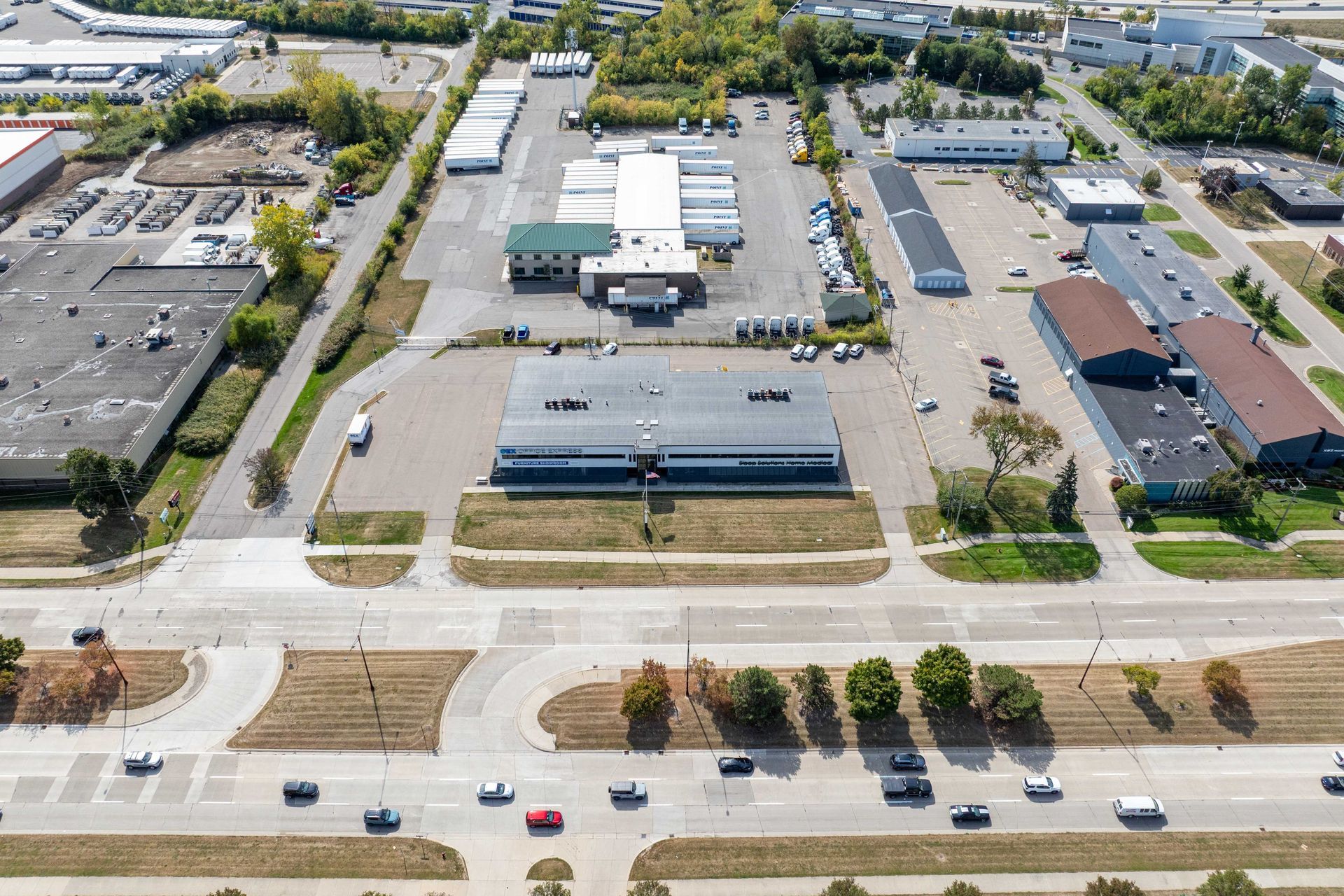 Aerial view of industrial buildings, paved lots, and a road with cars.