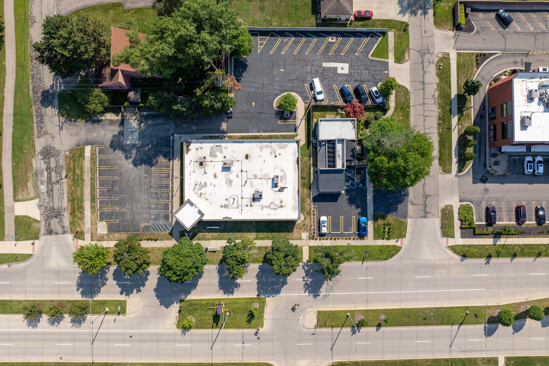 Aerial view of city block with buildings, roads, parking areas, and trees.