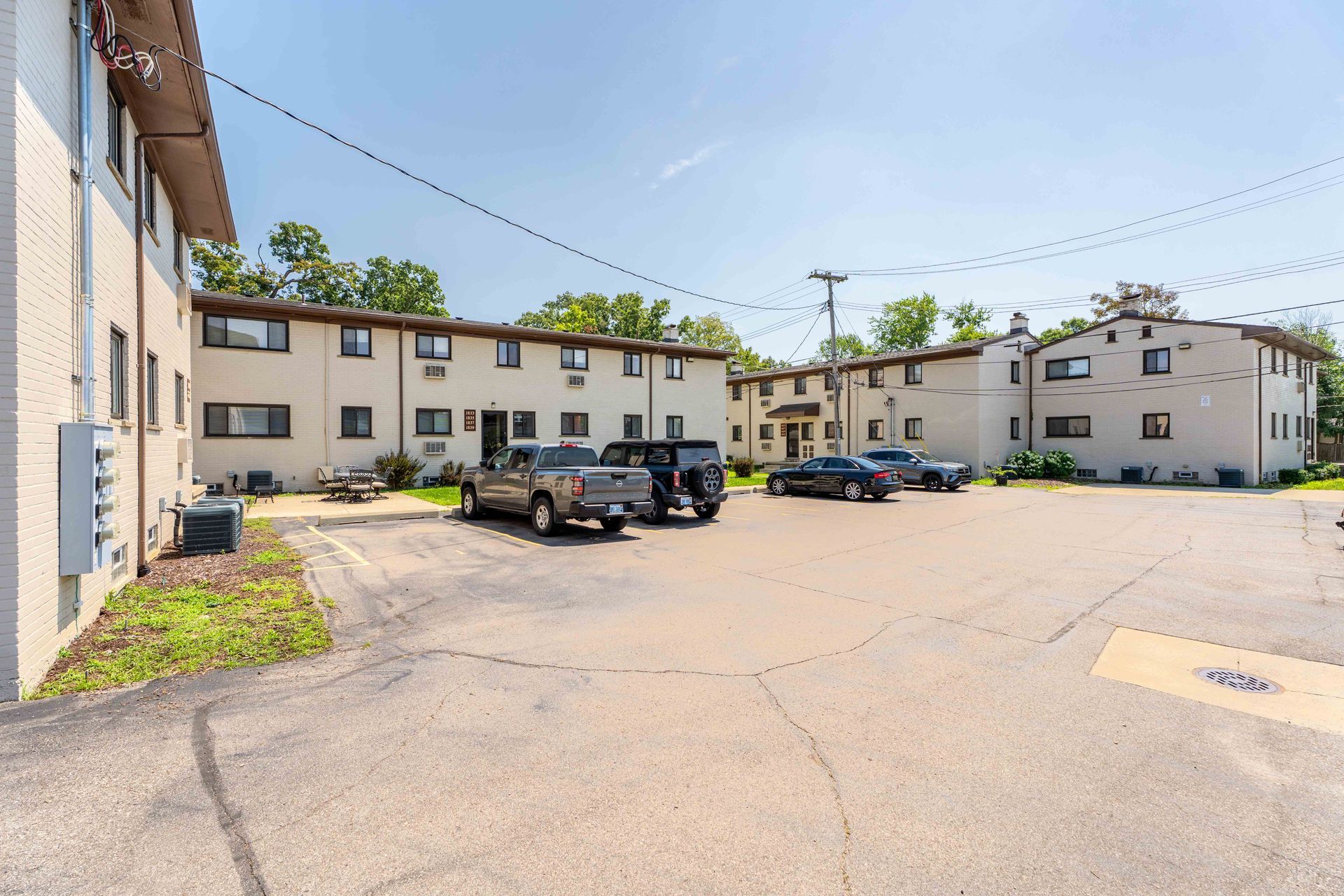 Apartment buildings with parked cars in a paved lot under a bright blue sky.