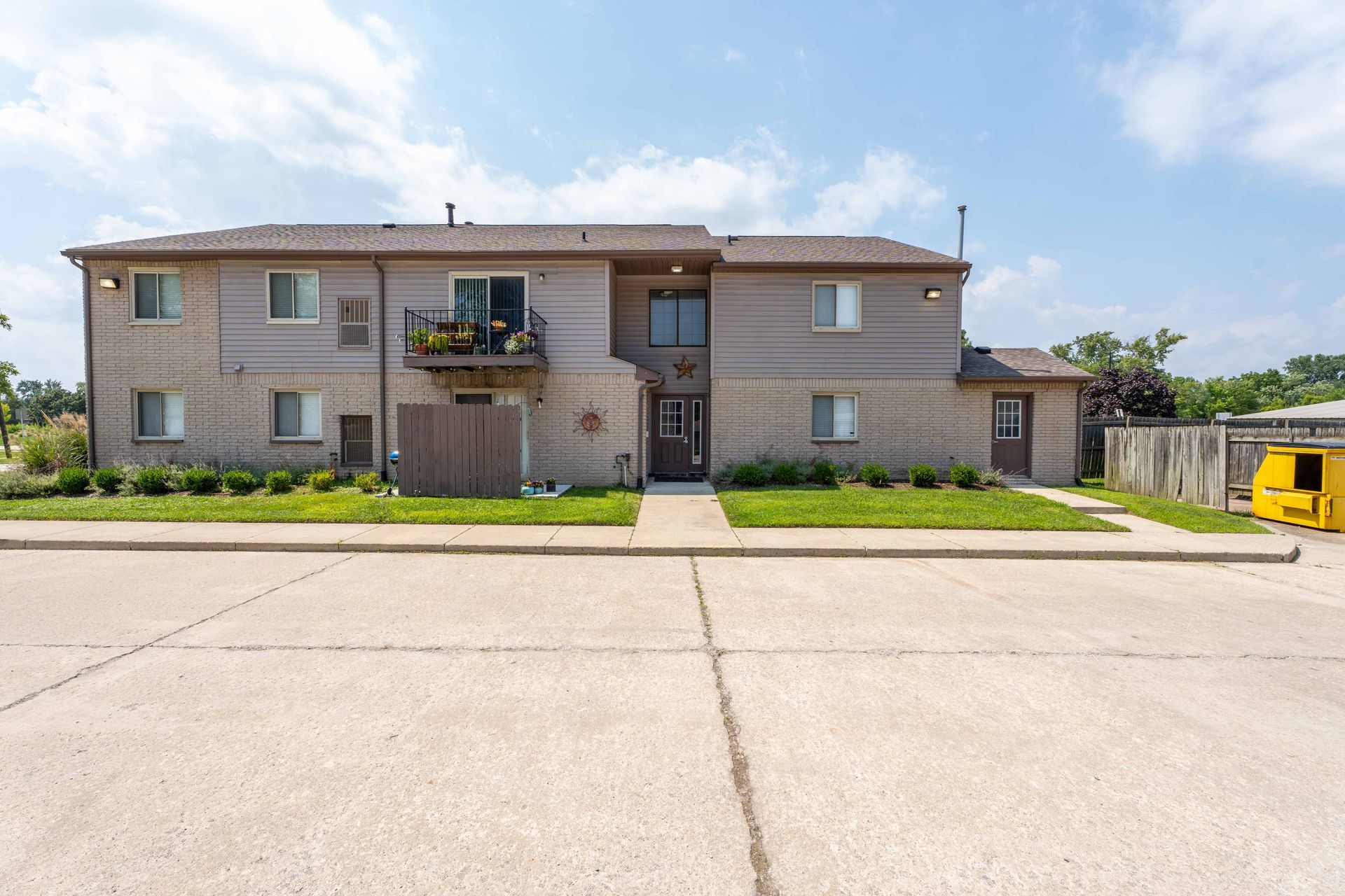 Two-story apartment building with a balcony and a paved parking lot.