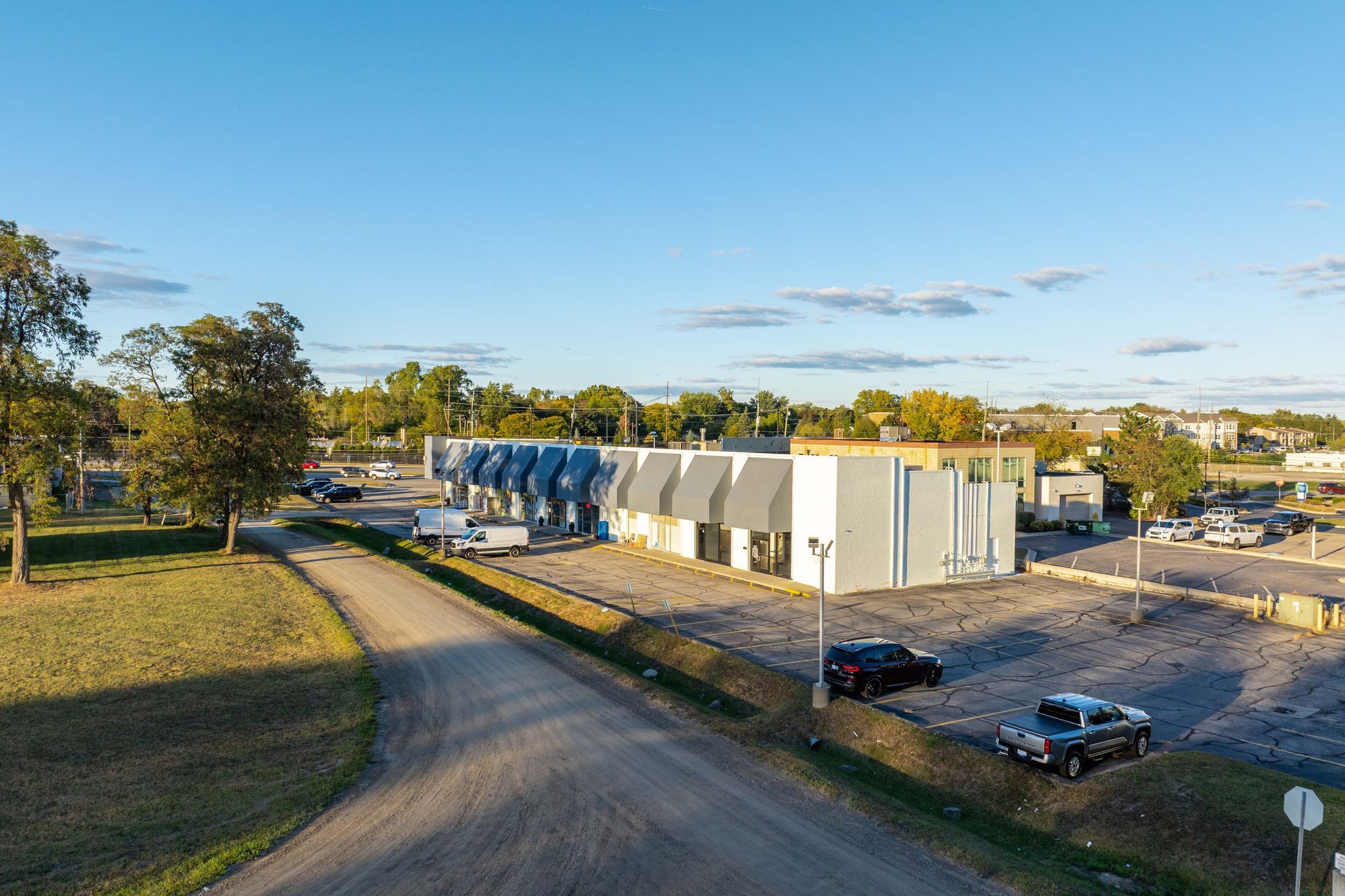 Building with blue tanks and gray roof, gravel lot, cars parked on a sunny day.