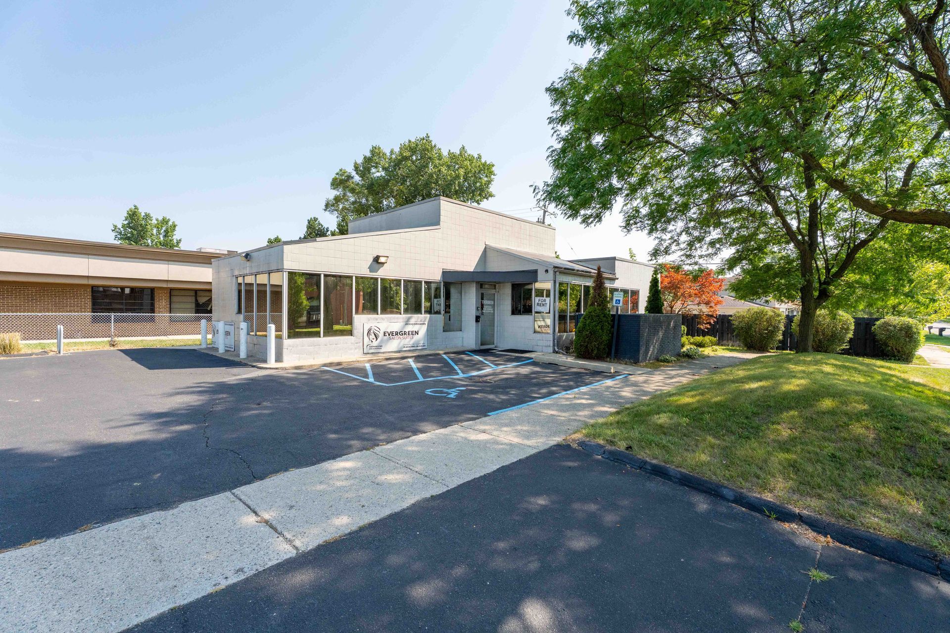 Exterior of a low, gray building with glass windows and a drive-through. Blue handicapped parking spot. Green lawn and trees.