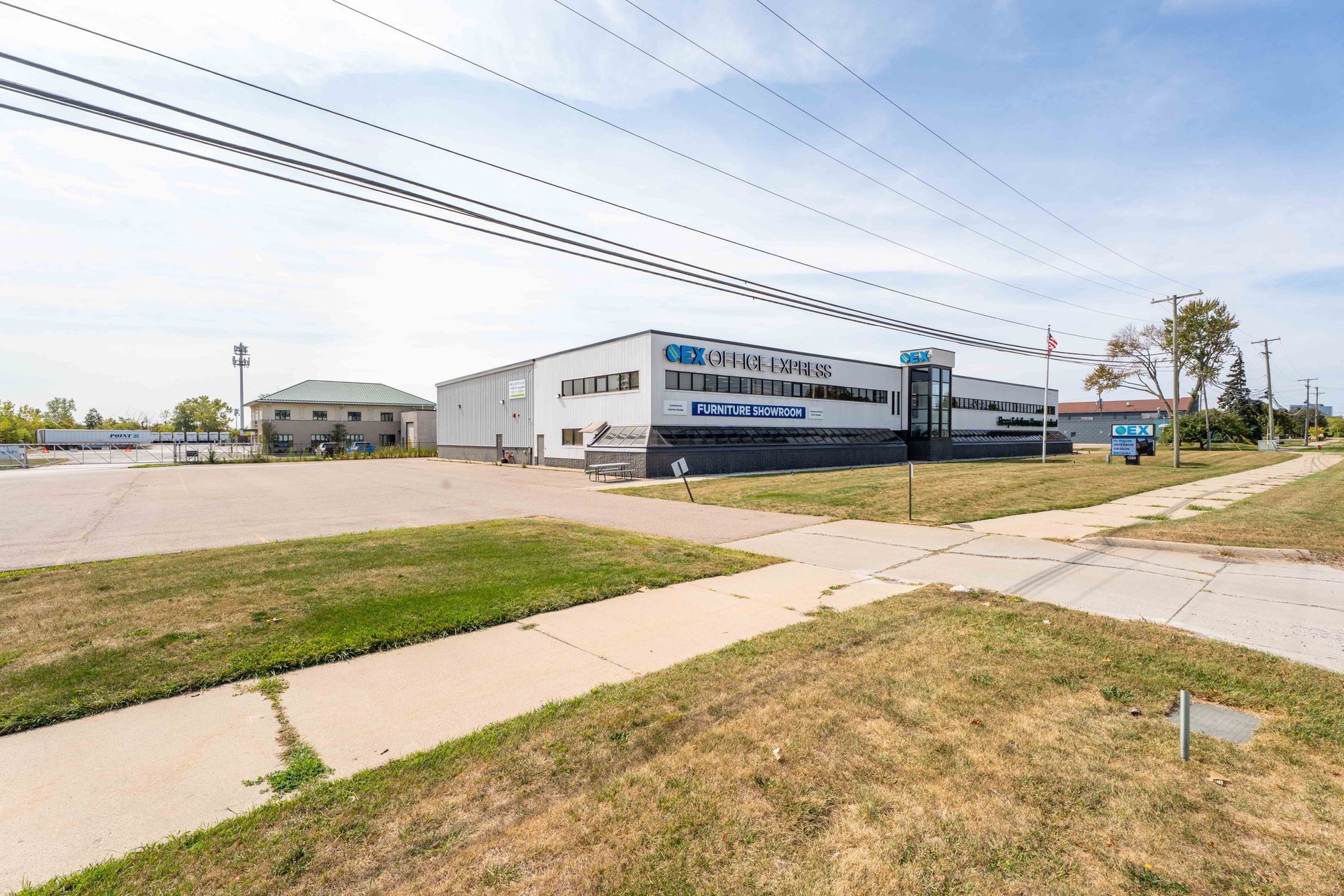 A low-angle view of a commercial building with blue and white signage, grassy surroundings, and overhead power lines.