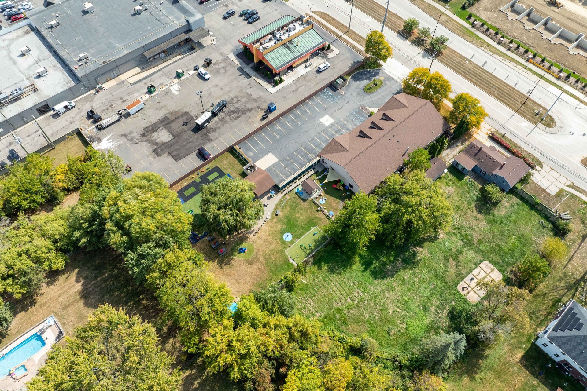 Aerial view of a hotel with a brown roof, a parking lot, and surrounding trees and grass.