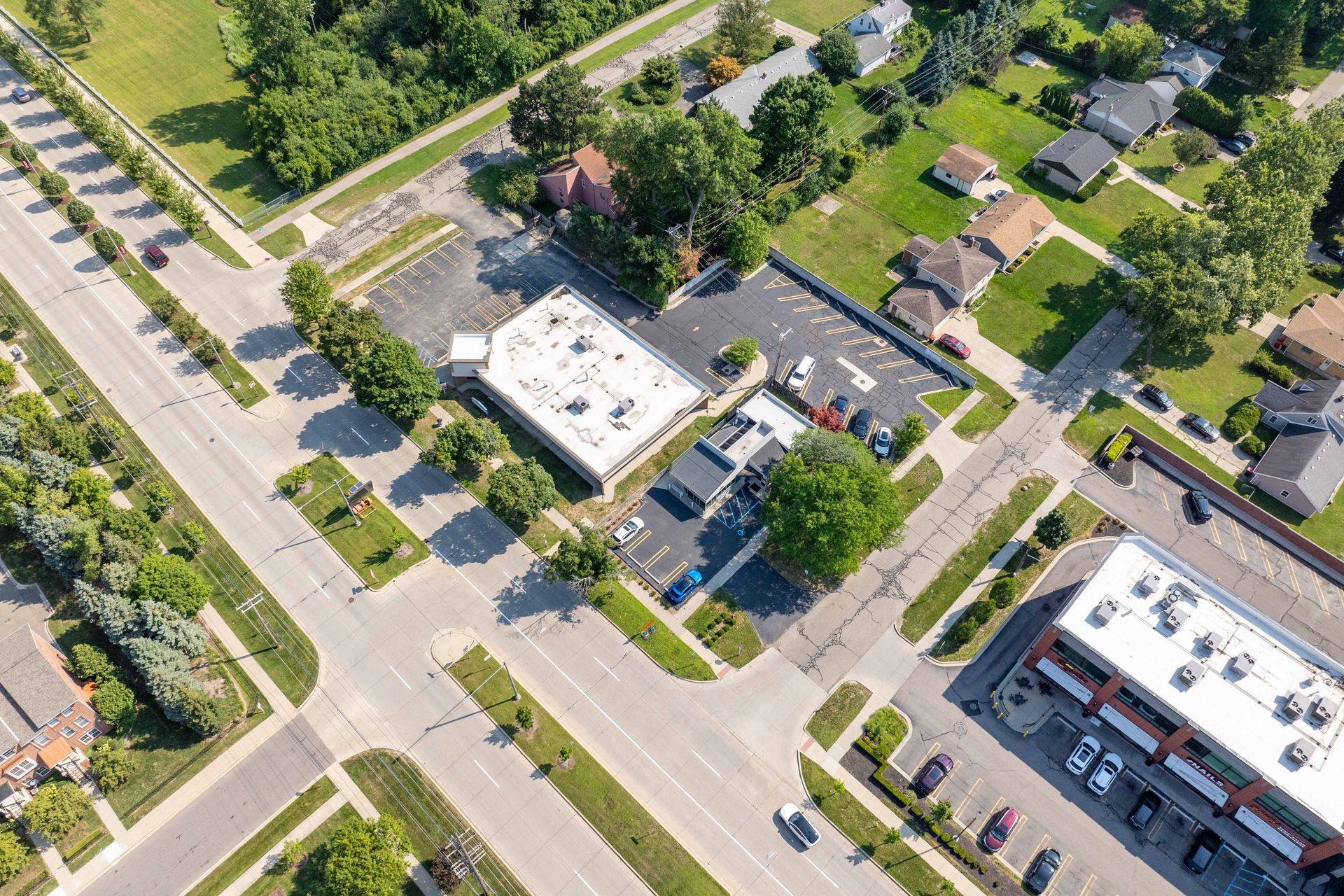 Aerial view of a commercial building with parking, adjacent to residential houses and roads lined with trees.