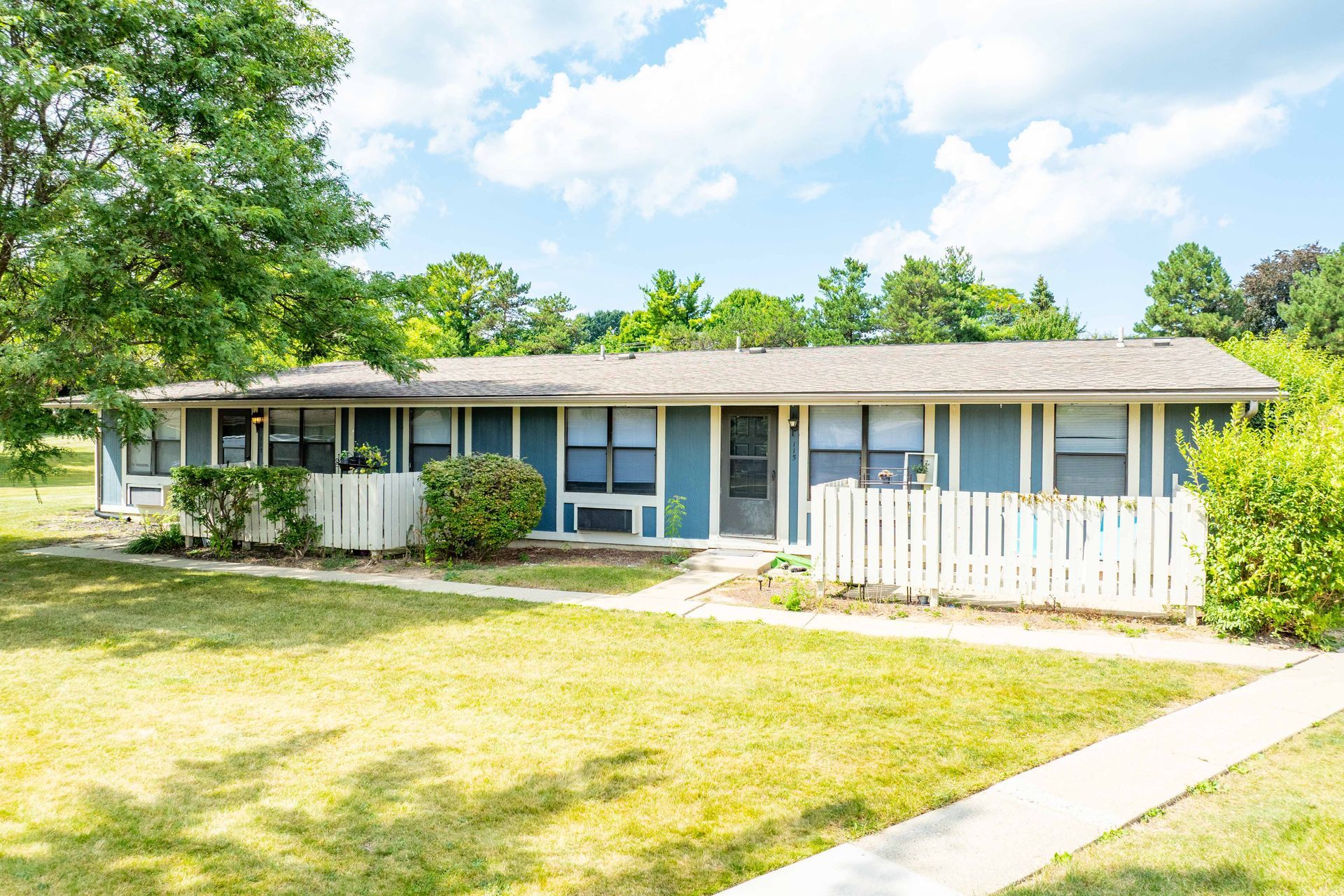Apartment building with blue siding, white fences, and green grass on a sunny day.