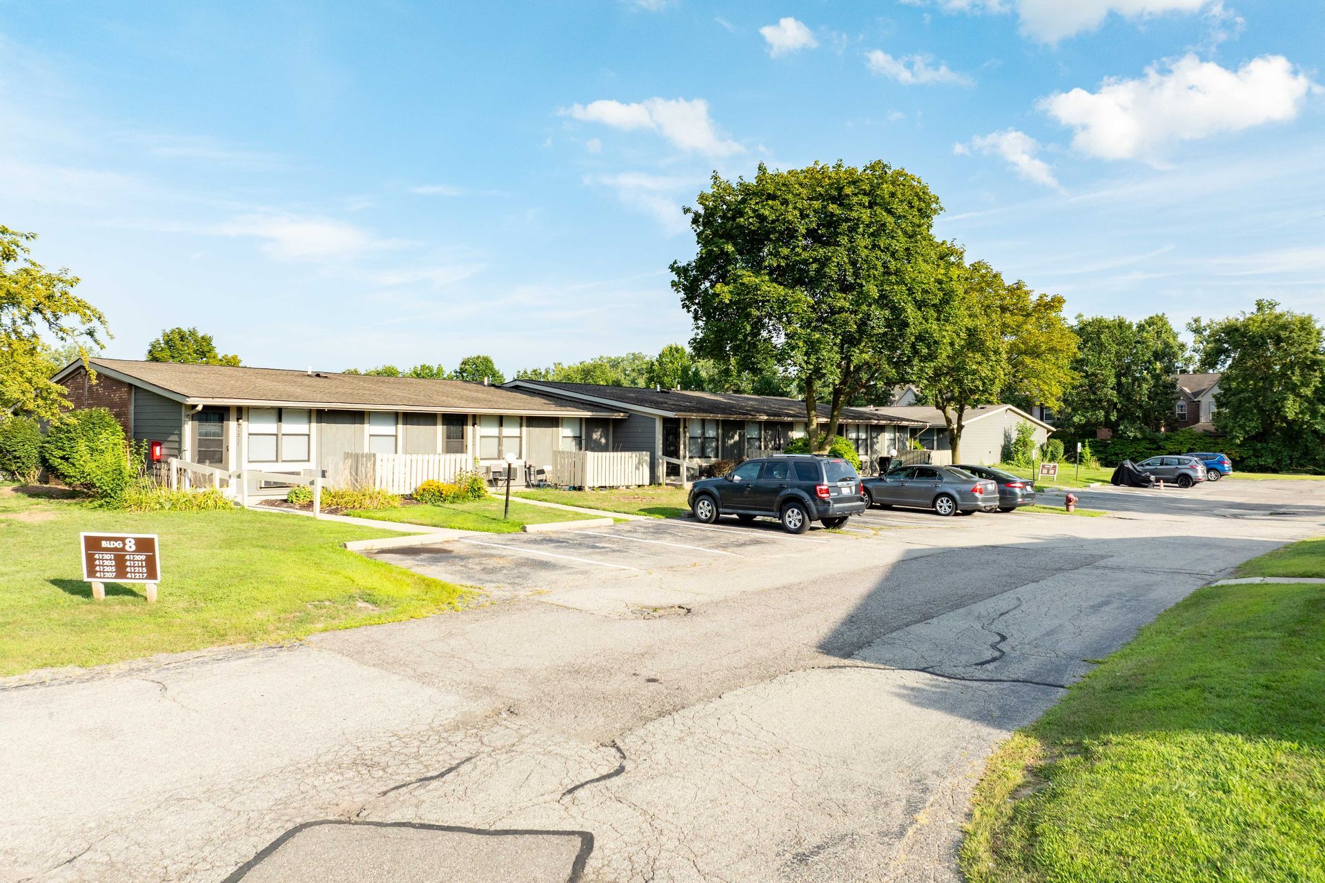 Apartment complex exterior with gray buildings, parking, green grass, and blue sky.