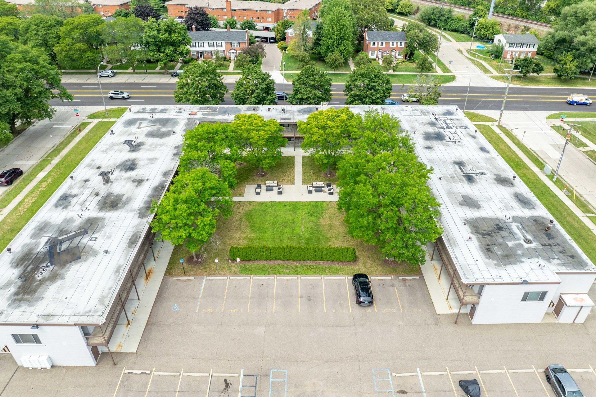 Aerial view of two connected apartment buildings with a courtyard and parking lot. Green trees and grass.
