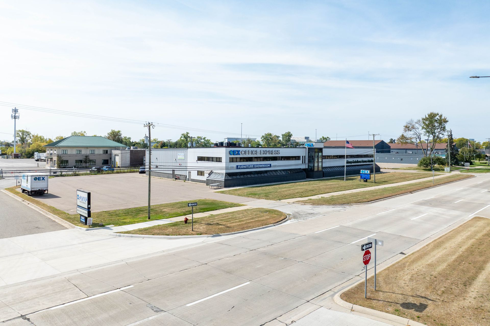 An aerial view of a white commercial building on a street corner, with parking lot and signage visible.