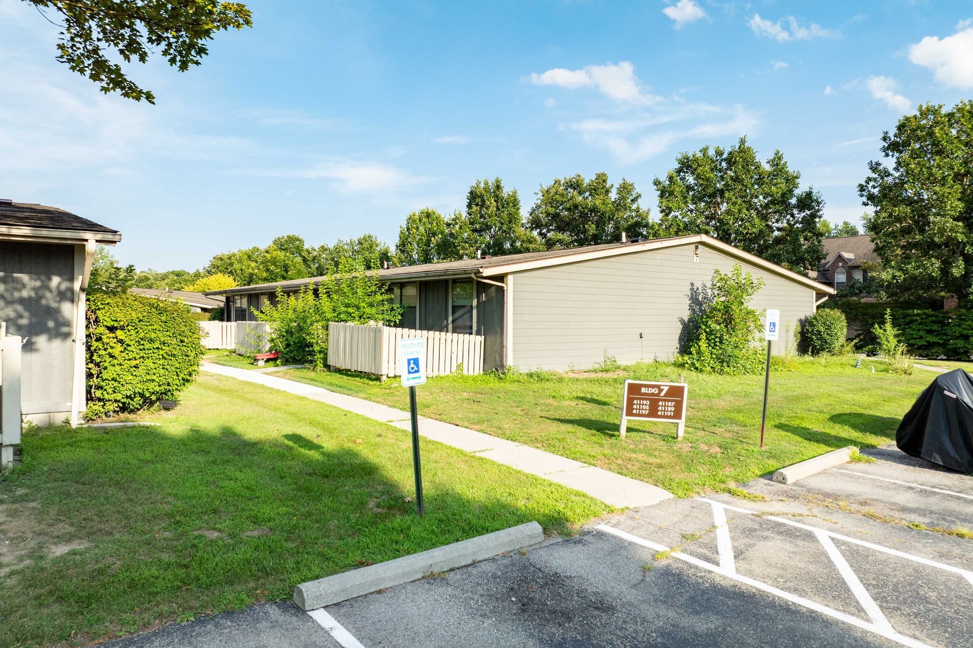 Exterior of apartments with accessible parking, green grass, and trees under a blue sky.