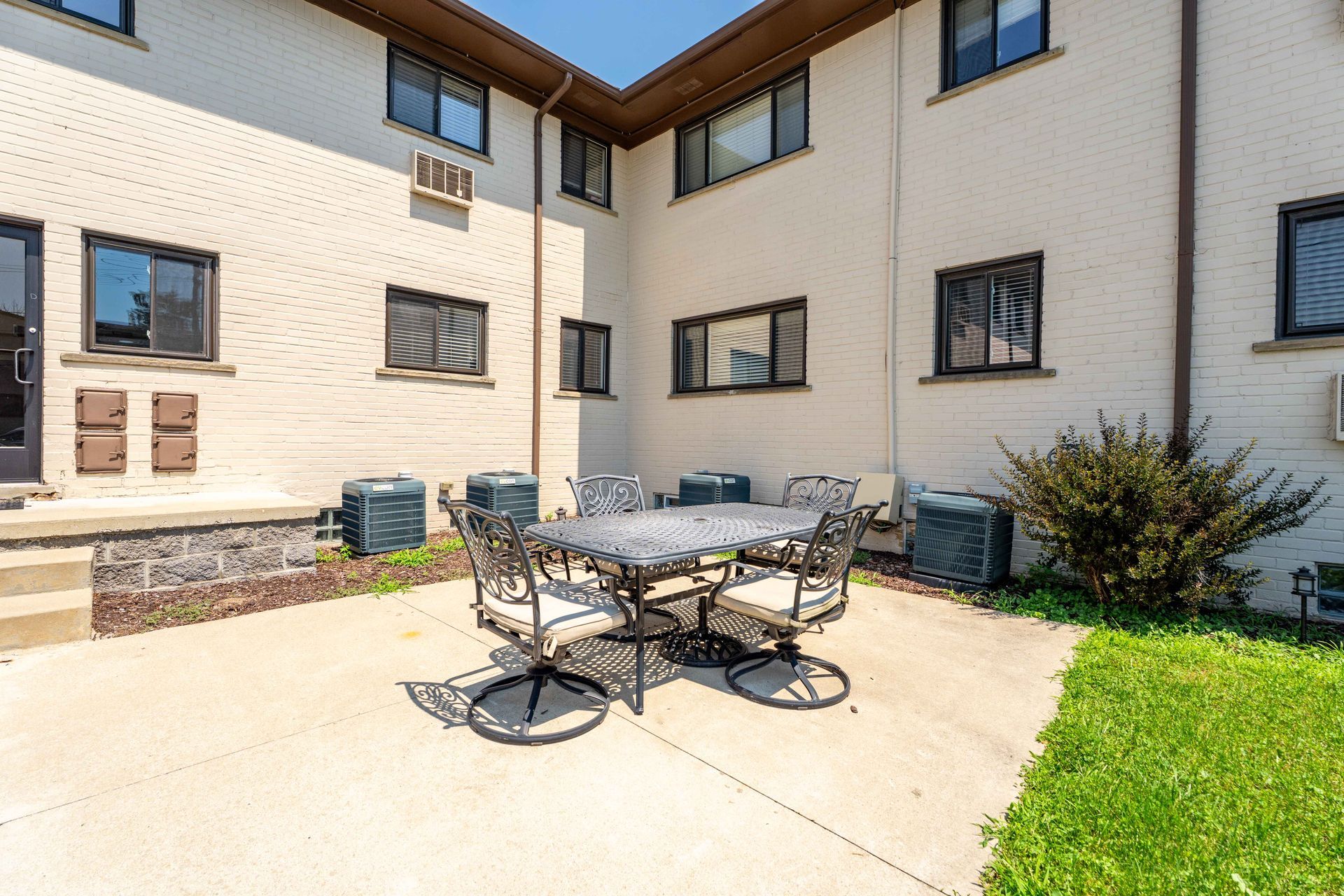 Patio with table and chairs in front of a brick apartment building on a sunny day.